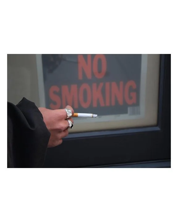 Close-up of a person's hand holding a cigarette with a 'No Smoking' sign in the background.
