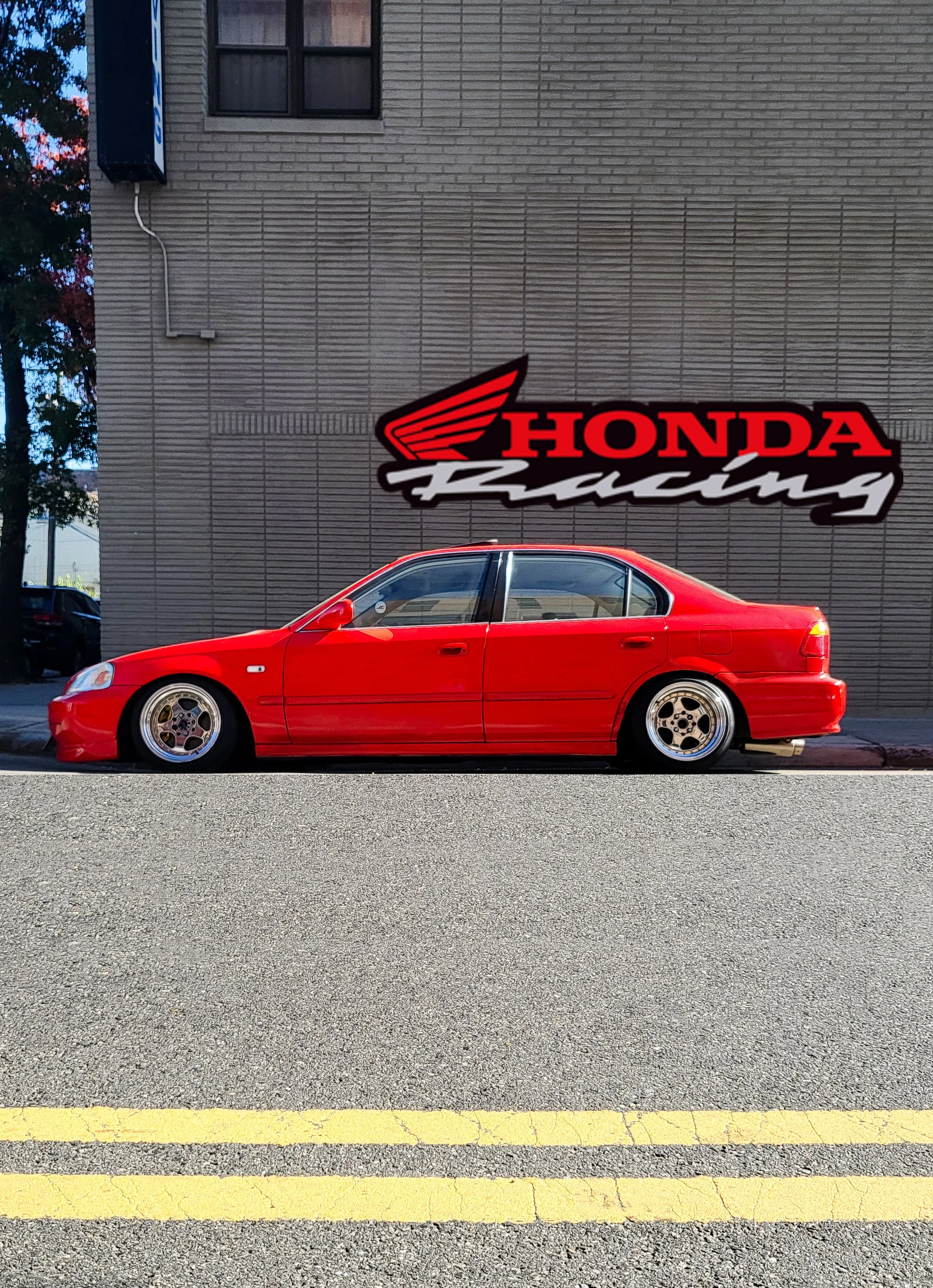 Red Honda Civic parked on the street in front of a brick wall with a Honda Racing sign.