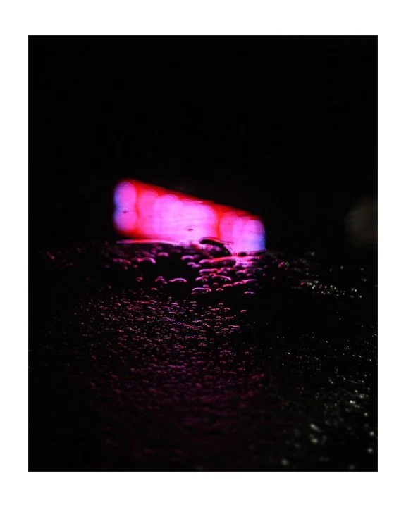 Close-up of a wet pavement reflecting pink and purple neon lights in the dark.