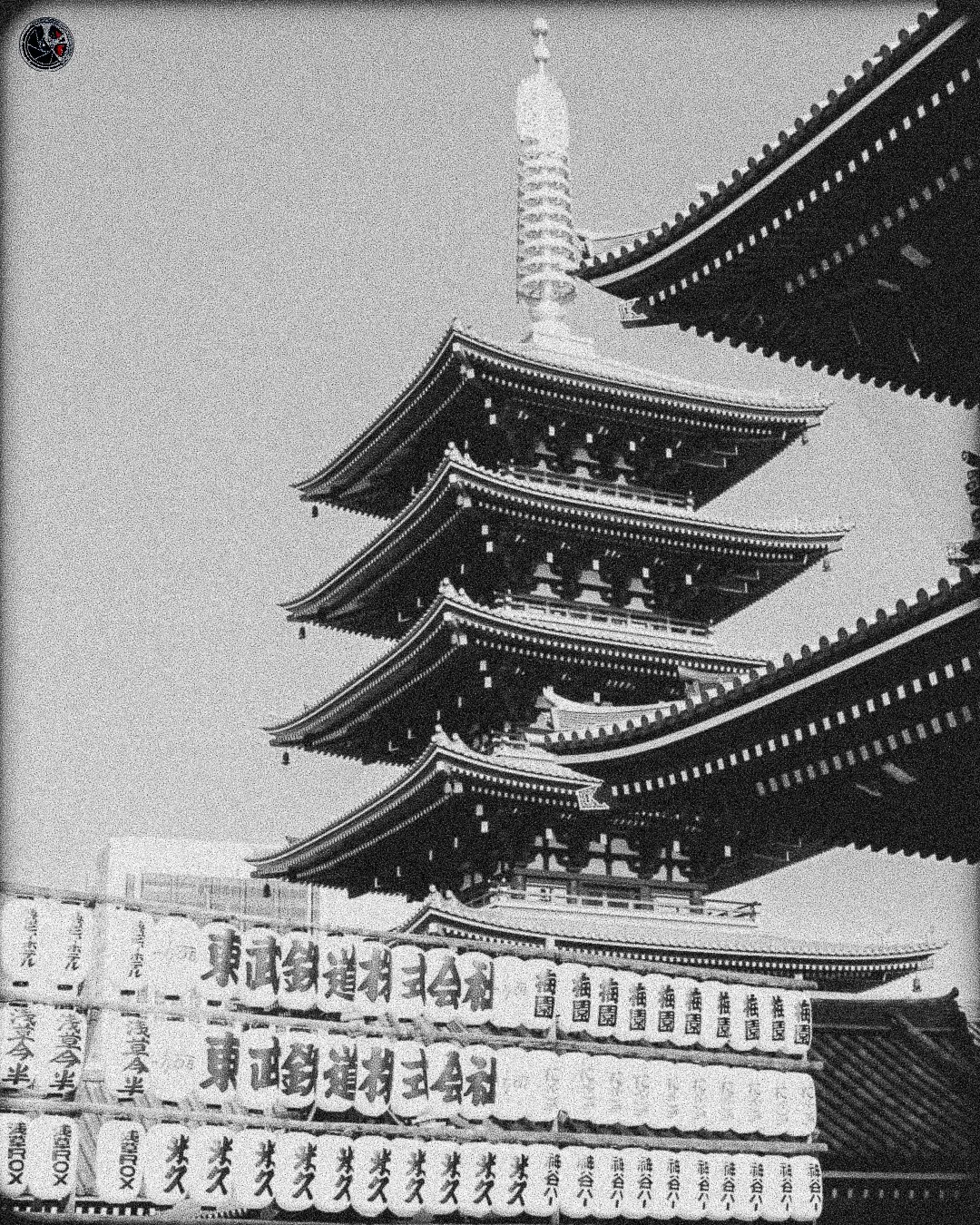 Black and white photo of a traditional Japanese pagoda with multiple tiers and ornate rooftops, with Japanese writings on a stone or wooden structure in the foreground.