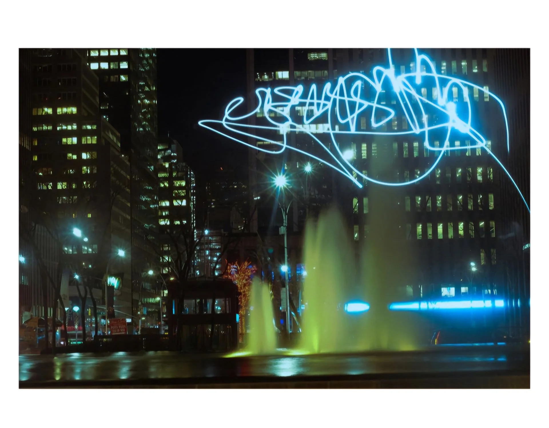 Night city scene with illuminated buildings, streetlights, a fountain with yellow-green water, and a blue graffiti tag in the sky.