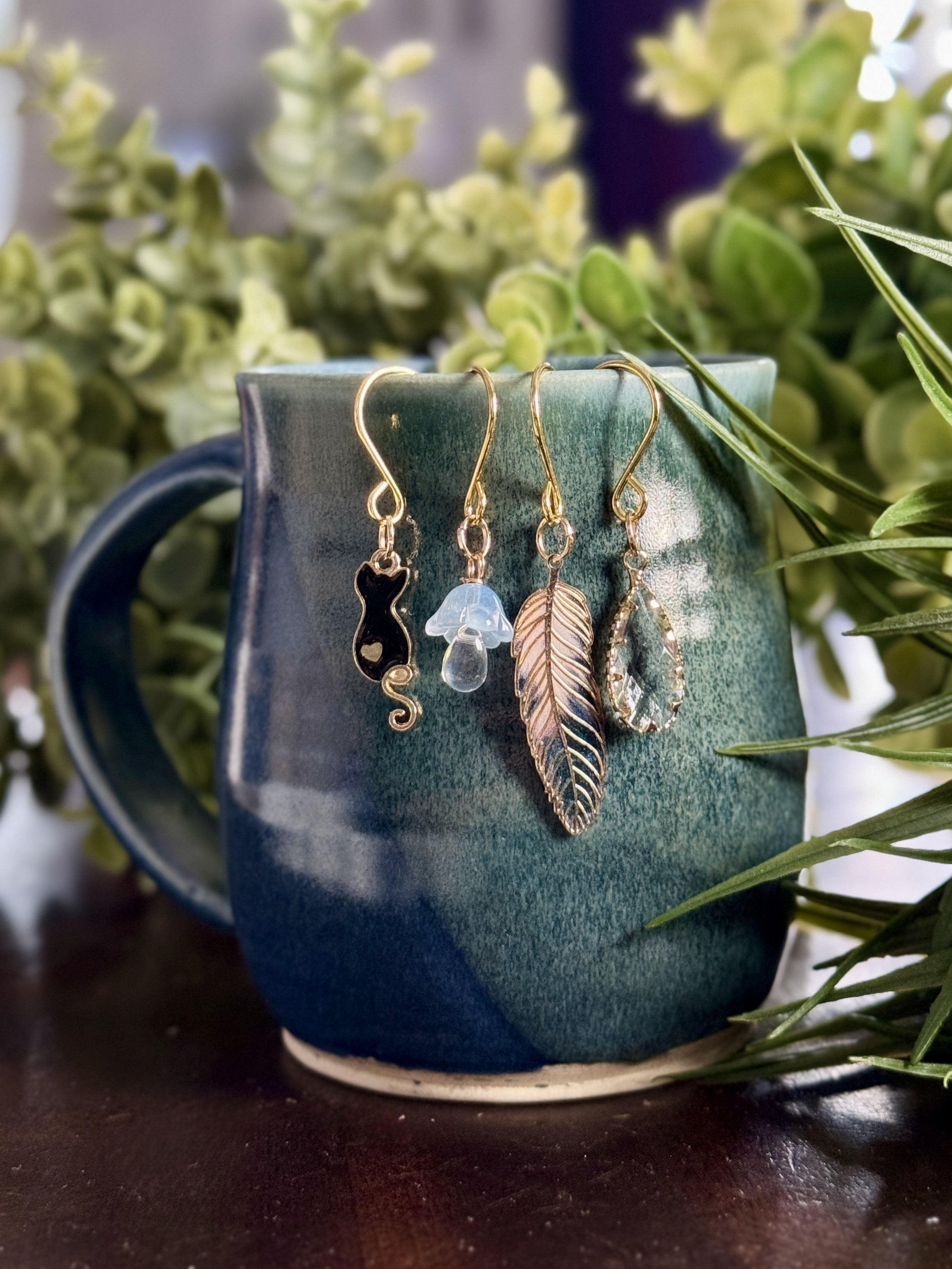 zoomed out front view of Black cat + feather + mushroom + crystal plant charms on a leafy background