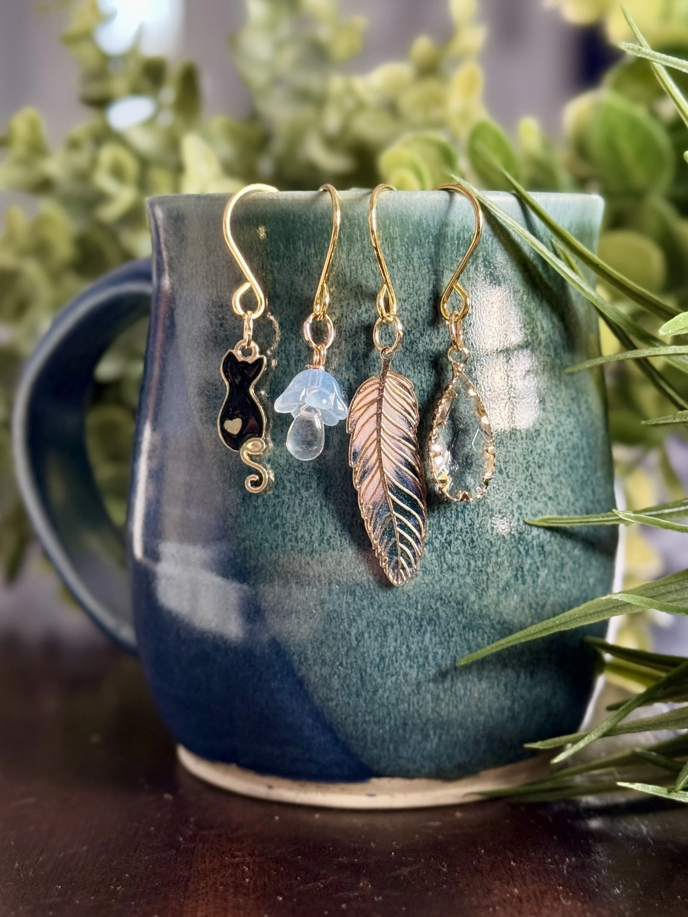 center front view of Black cat + feather + mushroom + crystal plant charms on a leafy background