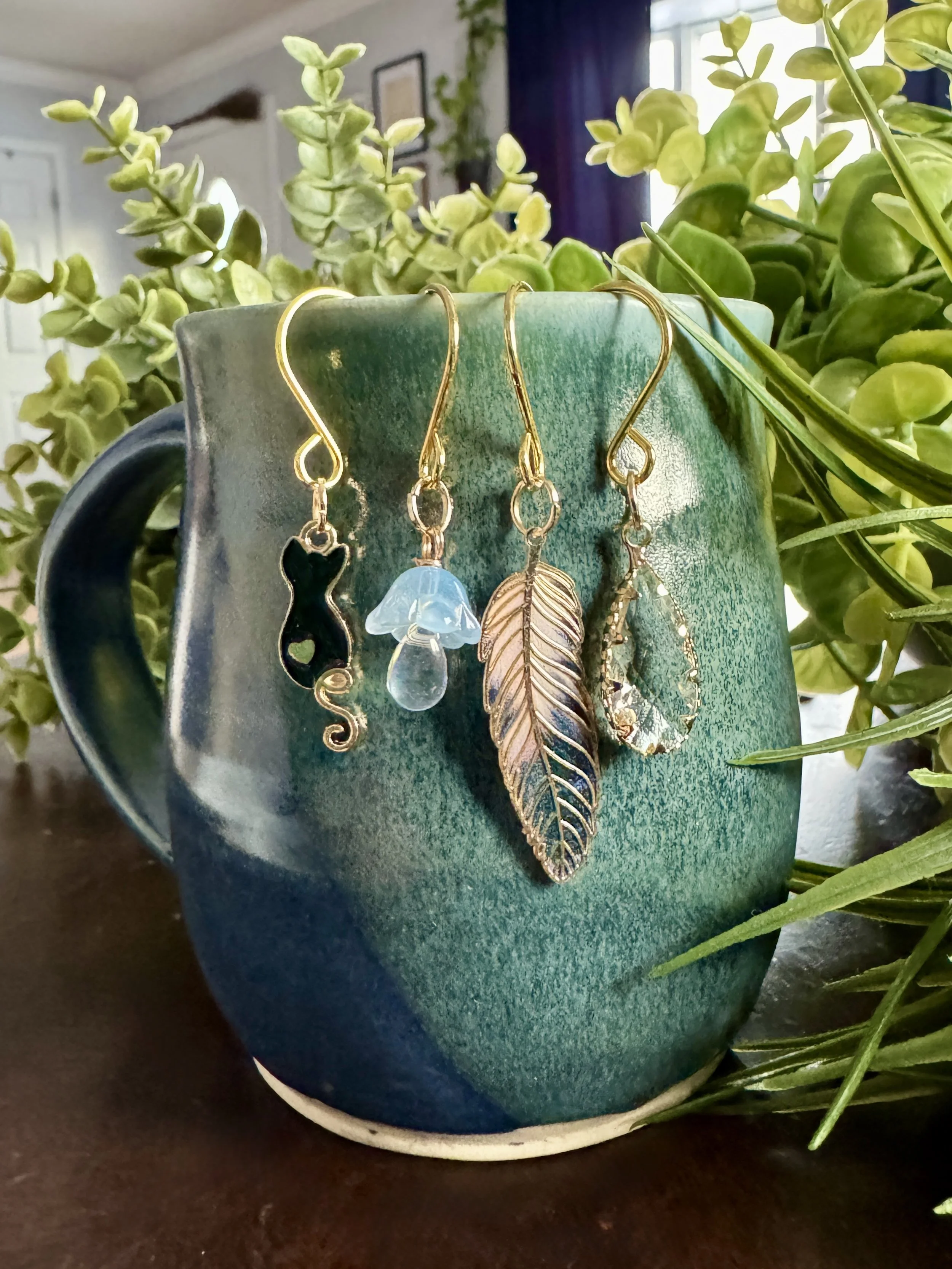 full front view of Black cat + feather + mushroom + crystal plant charms on a leafy background