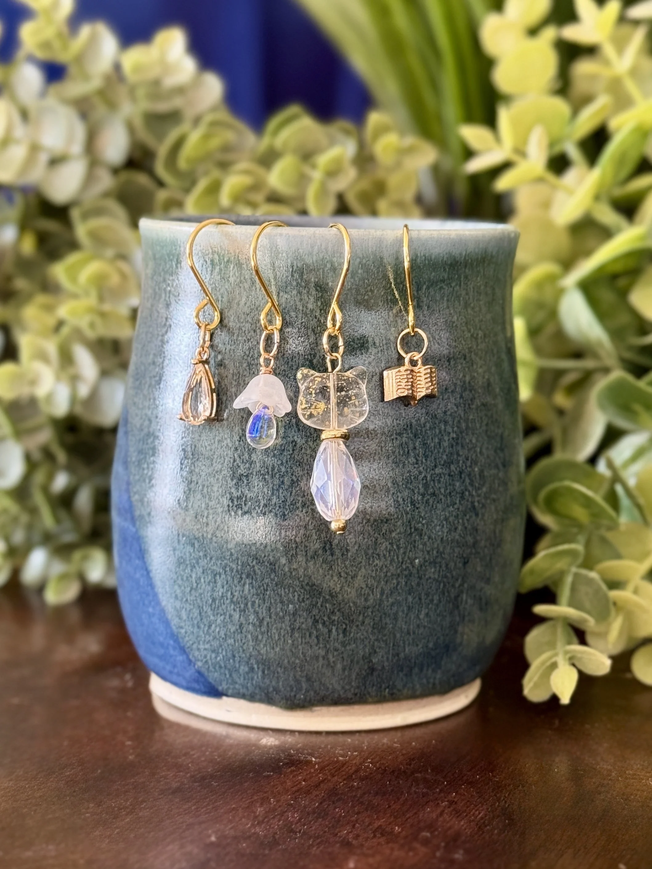 Front View of White cat + white mushroom + book + crystal pendant plant charm set on a mug with a leafy background