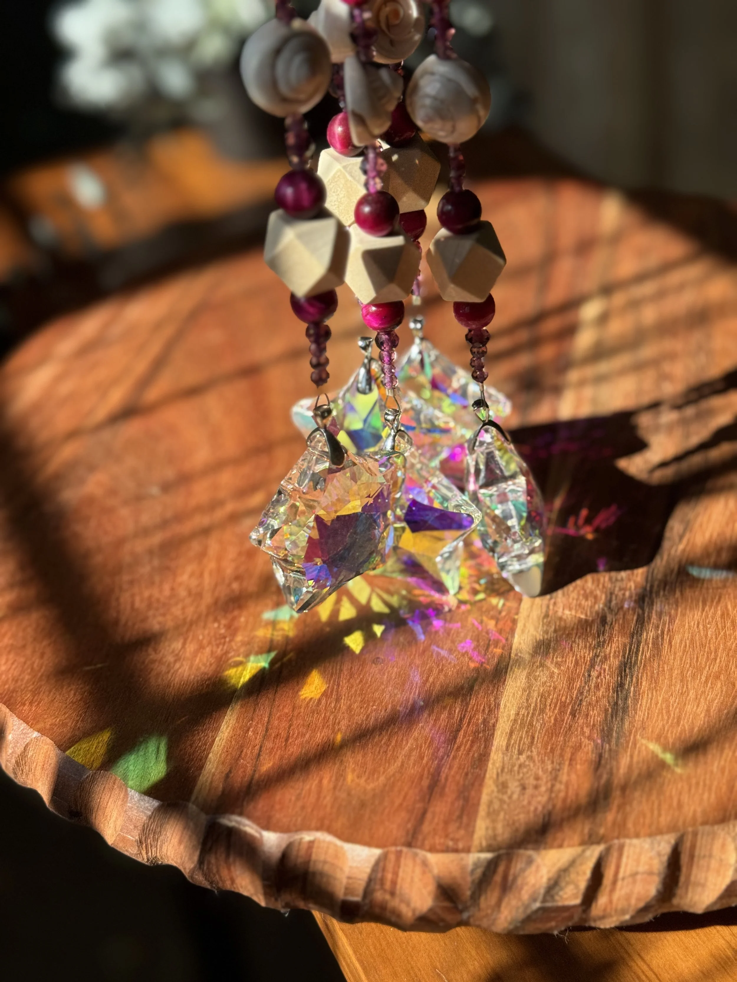 Close-up of hanging crystal ornaments reflecting colorful light patterns onto a wooden surface, with beads and shells at the top.
