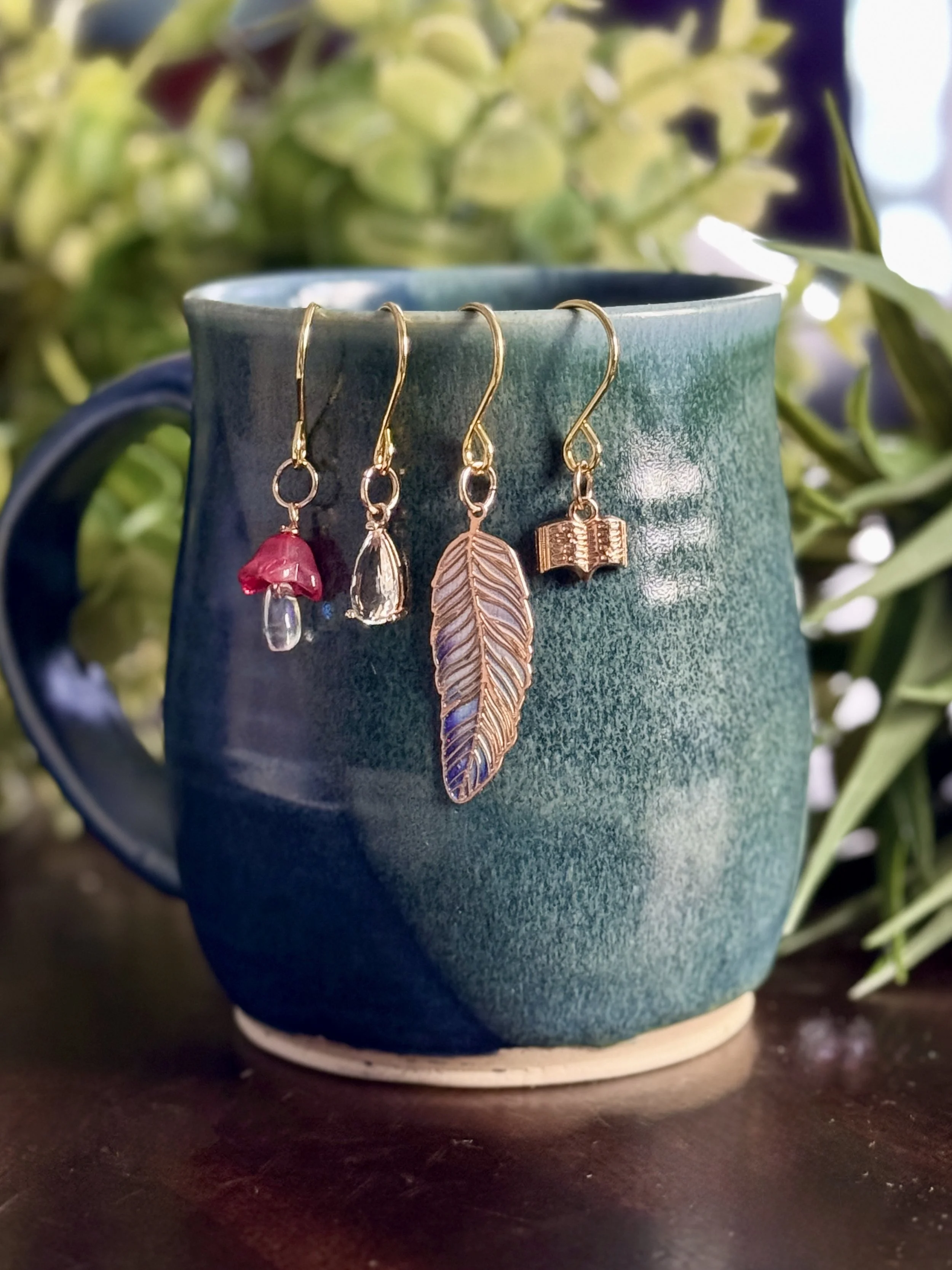 5th Alternative front view of a pink mushroom + book + feather + crystal plant charms hanging on a mug with leafy background