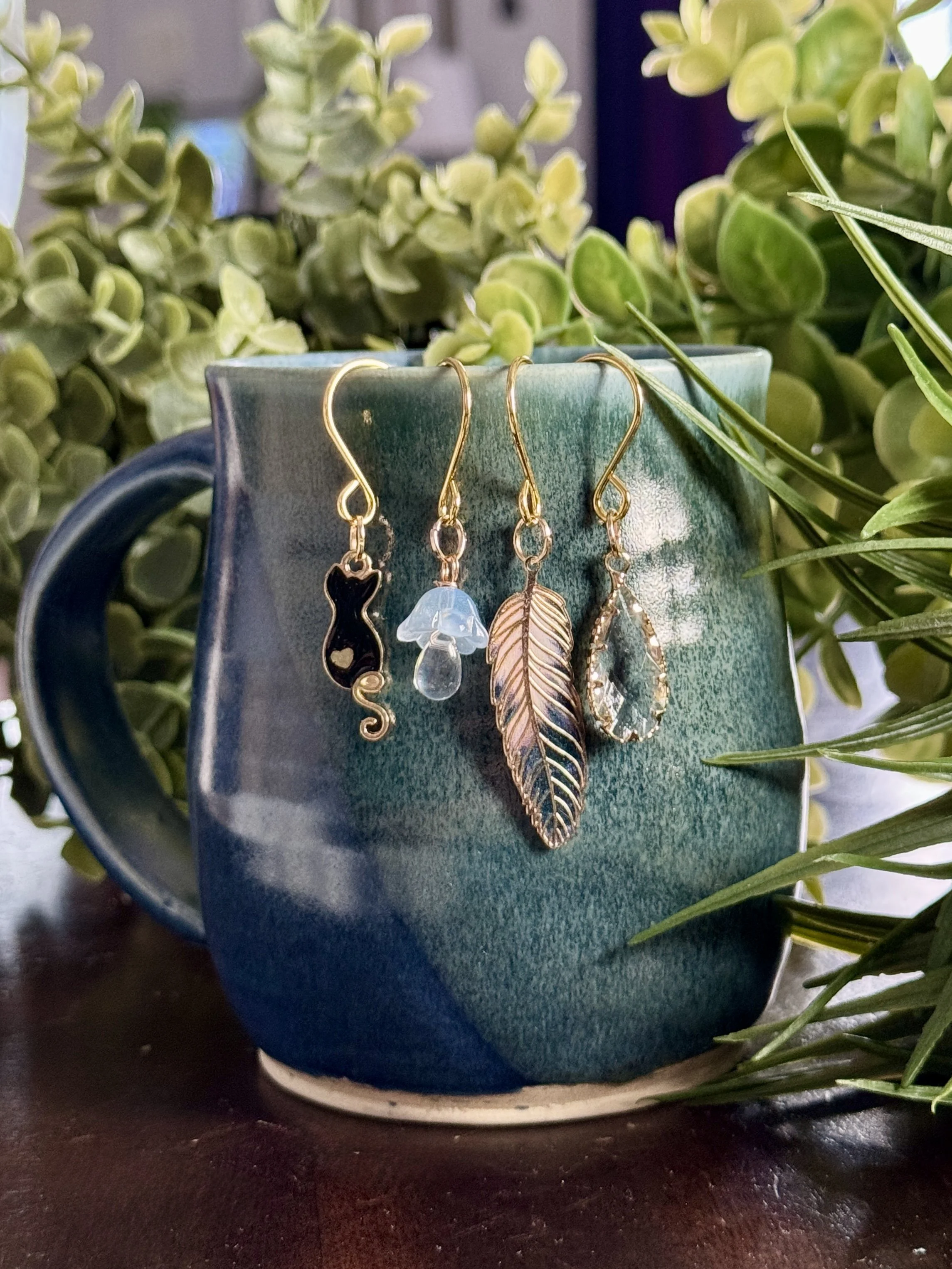 slightly top down front view of Black cat + feather + mushroom + crystal plant charms on a leafy background
