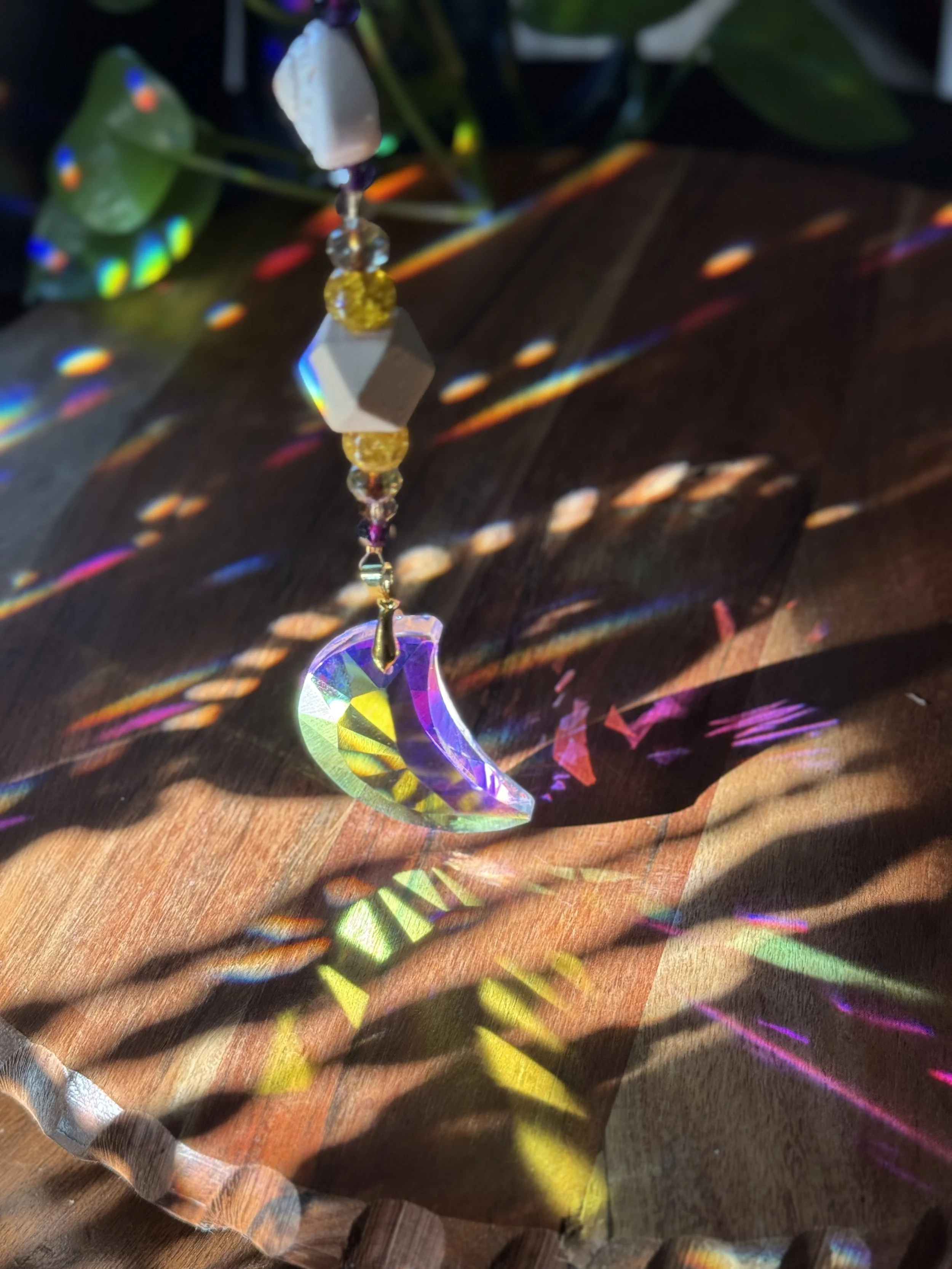 A sun catcher with beads and a crescent moon-shaped crystal, creating colorful light reflections on a wooden surface.