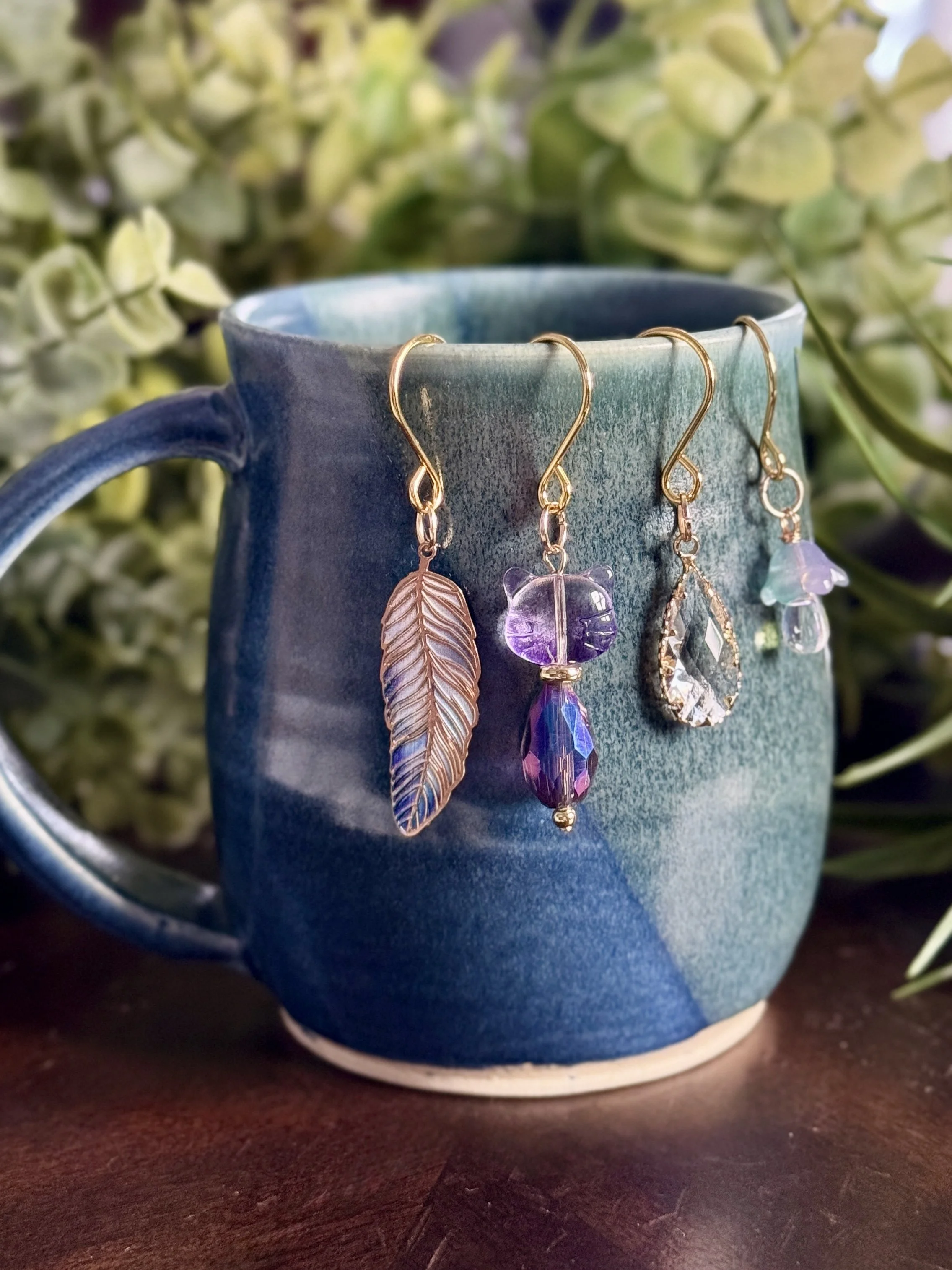 3rd alternative front View of Purple cat + lavender mushroom + feather + crystal plant charms on a blue mug with leafy background