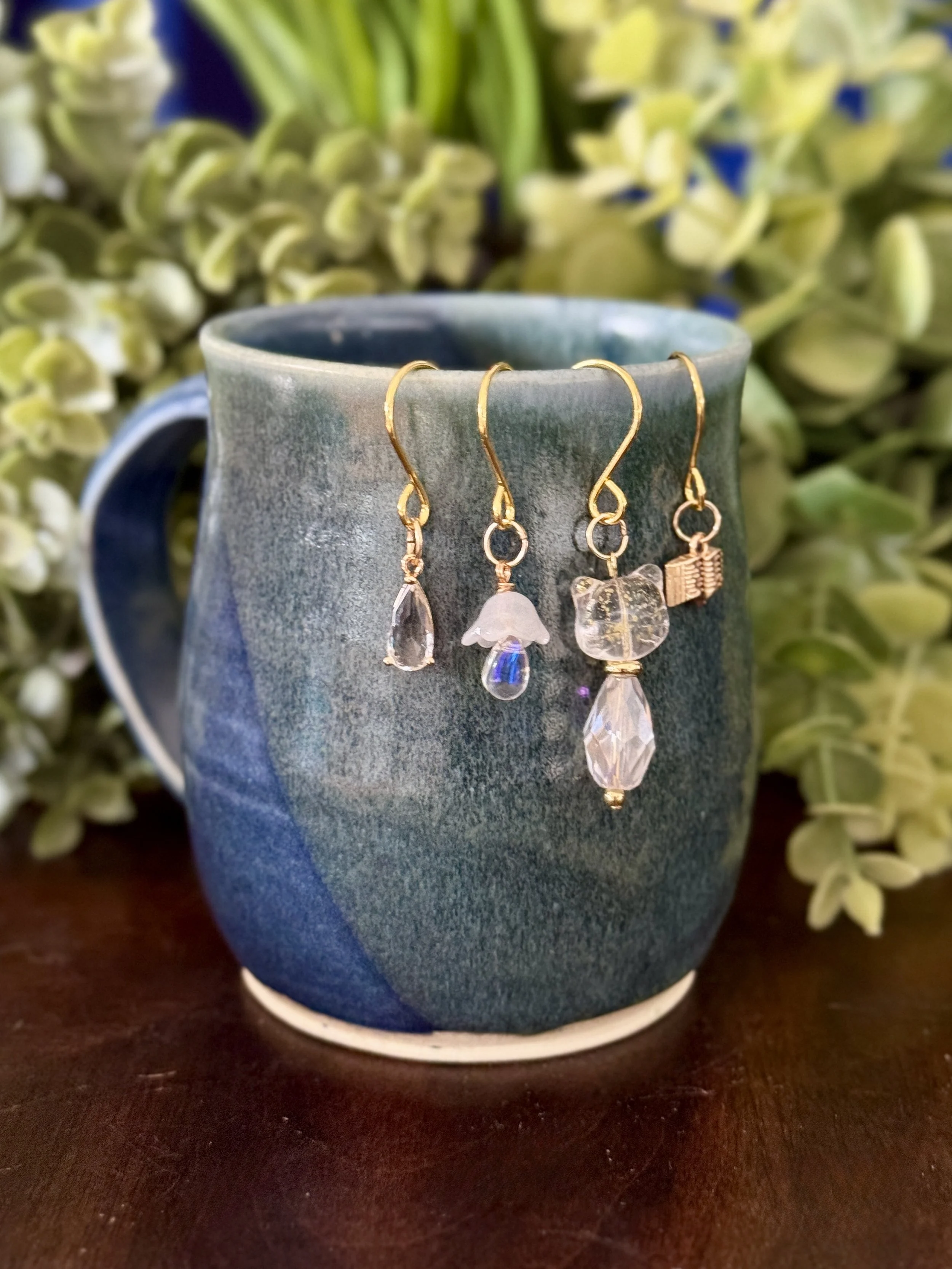 5th Front View of White cat + white mushroom + book + crystal pendant plant charm set on a mug with a leafy background