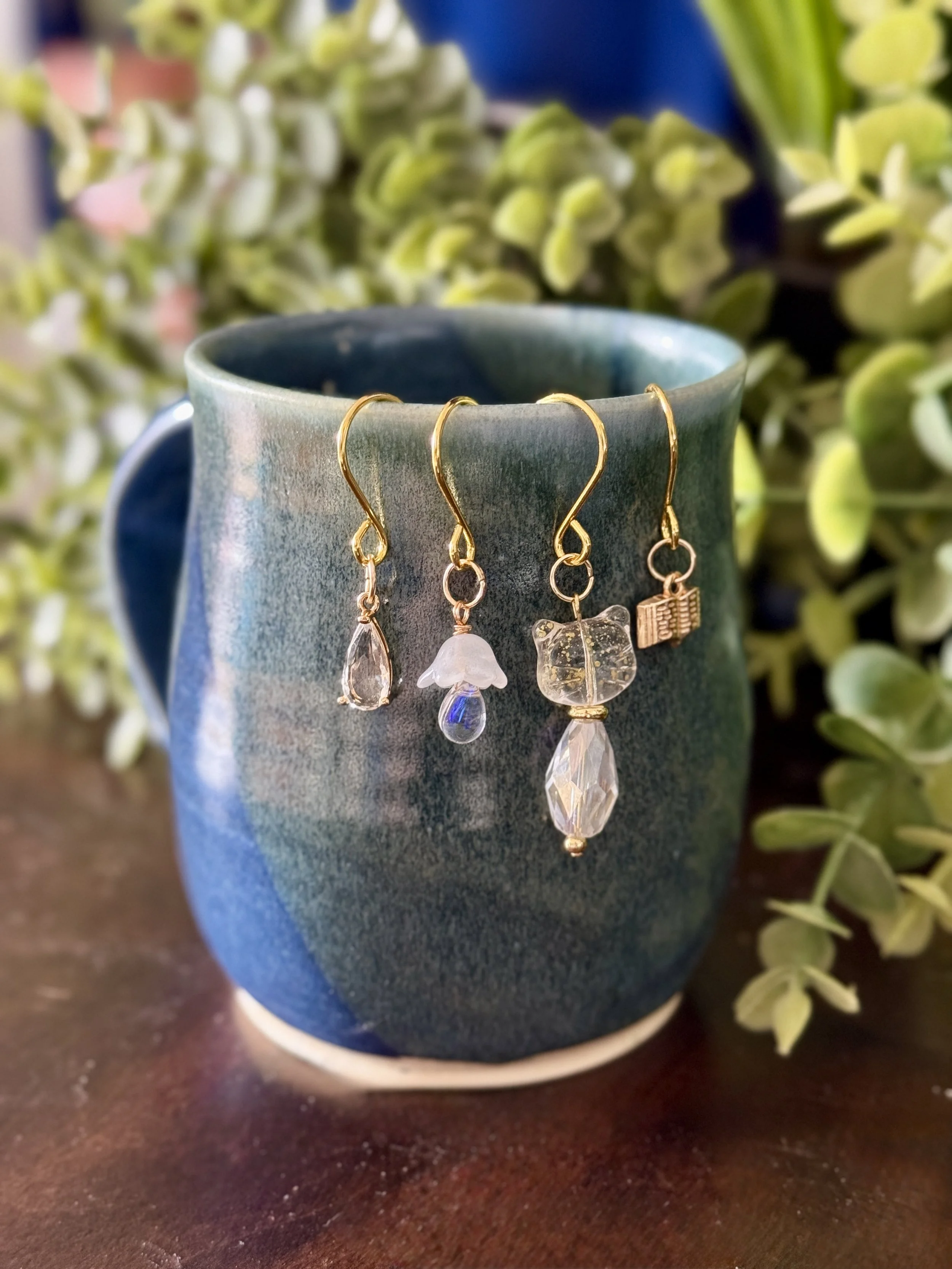 4th Front View of White cat + white mushroom + book + crystal pendant plant charm set on a mug with a leafy background