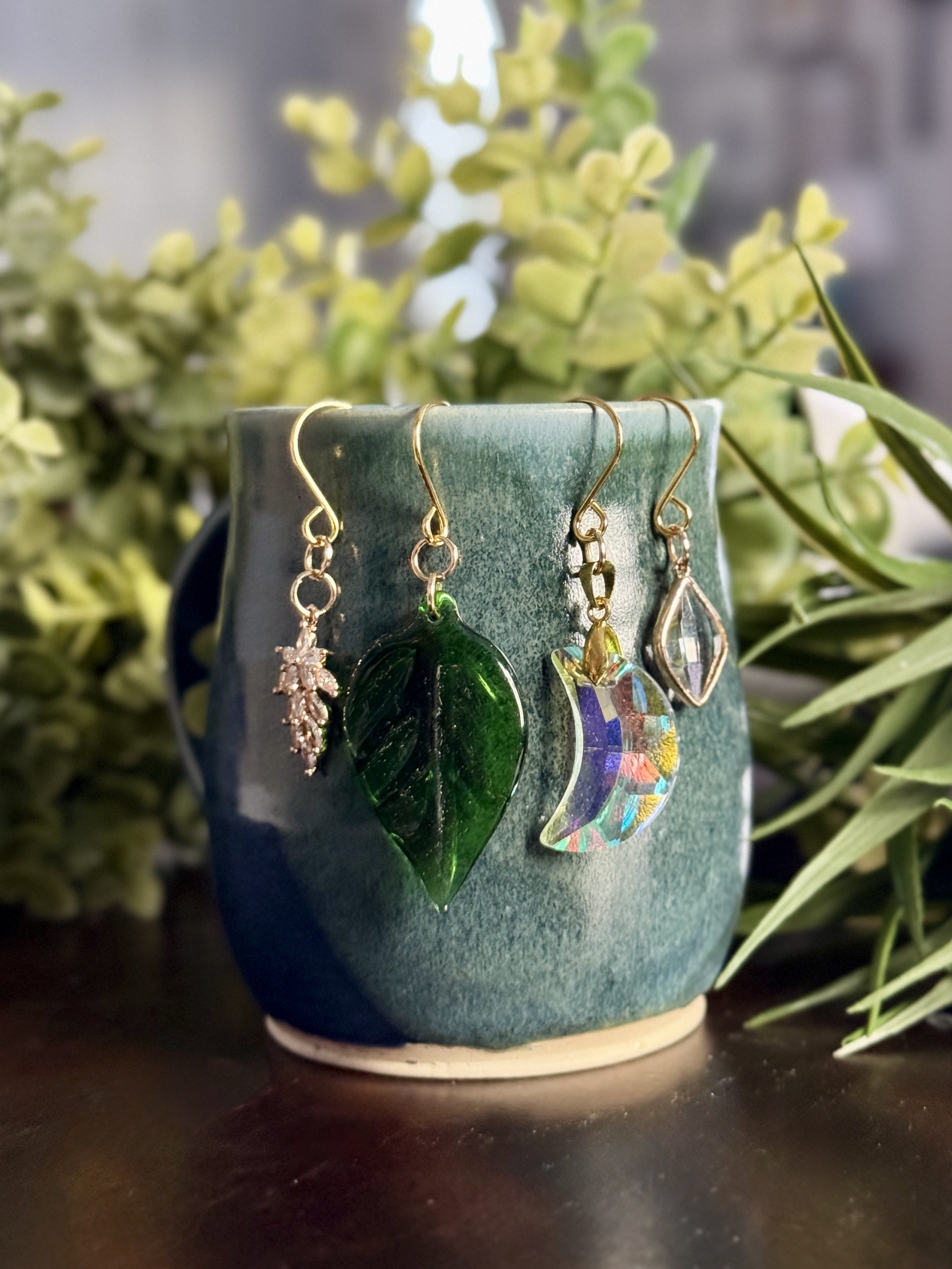 Front View of Crystal moon + antique glass leaf + 2 crystal pendant plant charms of a mug with leafy background