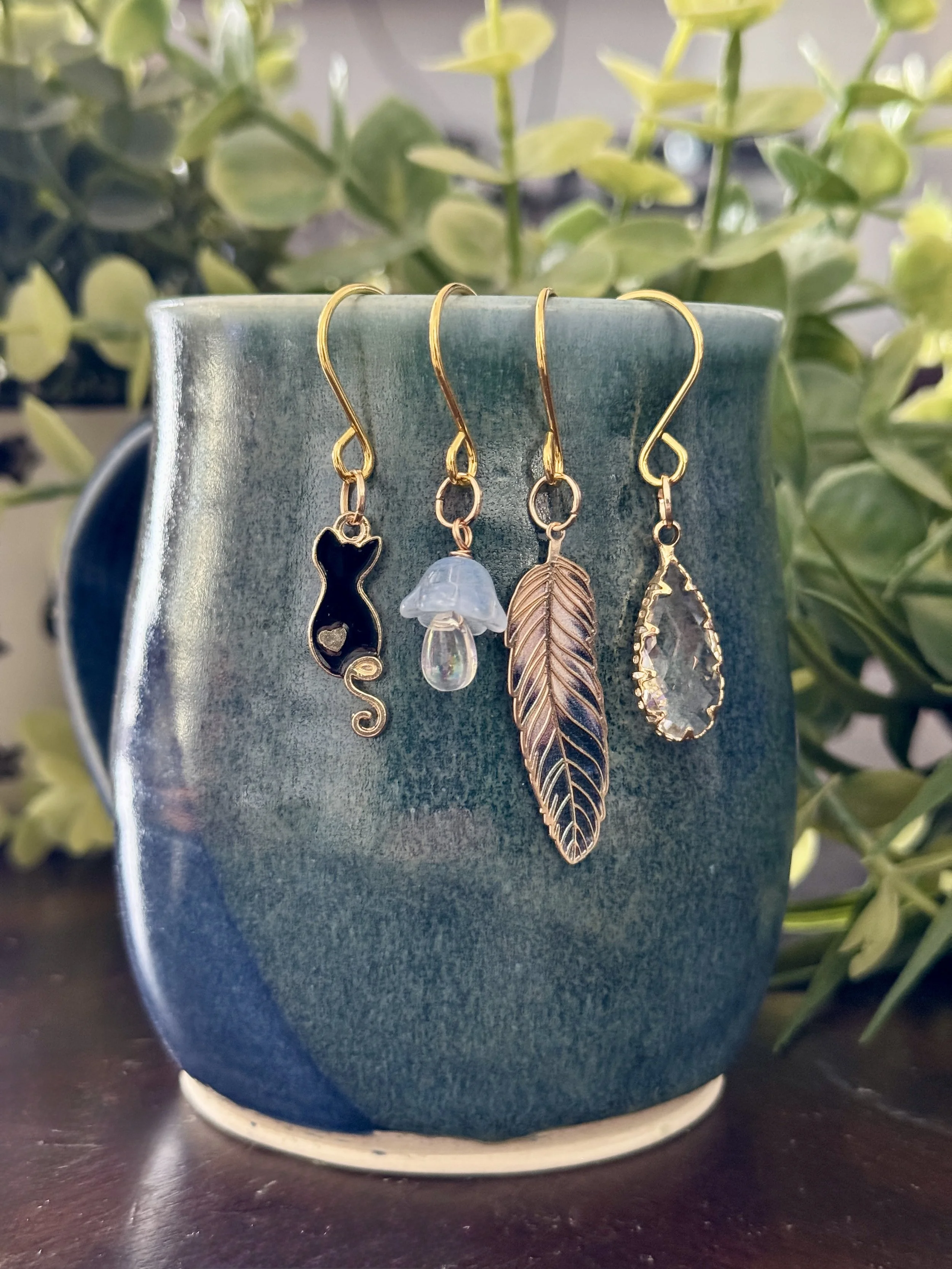 Alternative front view of Black cat + feather + mushroom + crystal plant charms on a leafy background