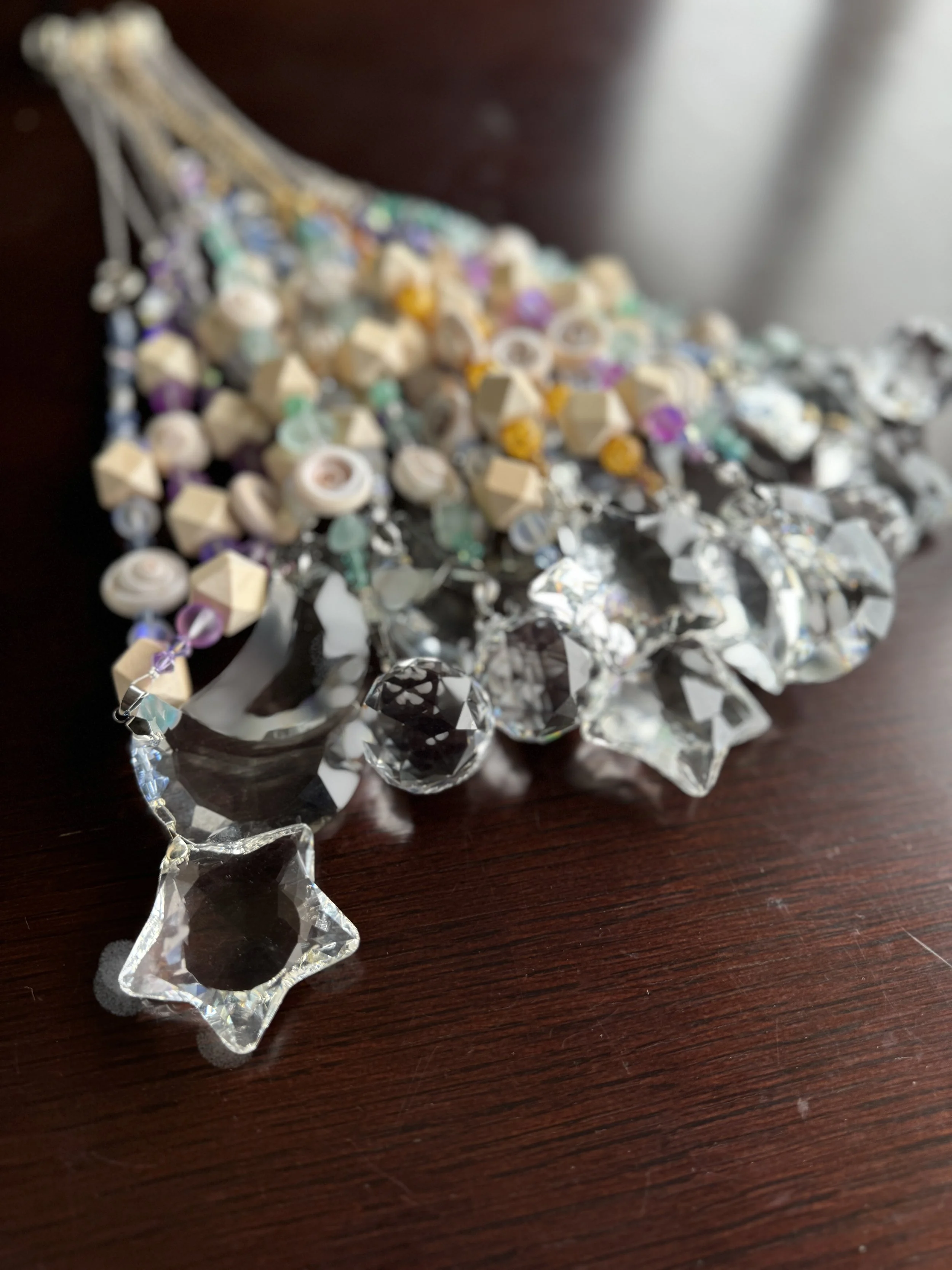 A beaded jewelry piece with various geometrically shaped beads, including clear and opaque ones, arranged on a dark wooden surface.