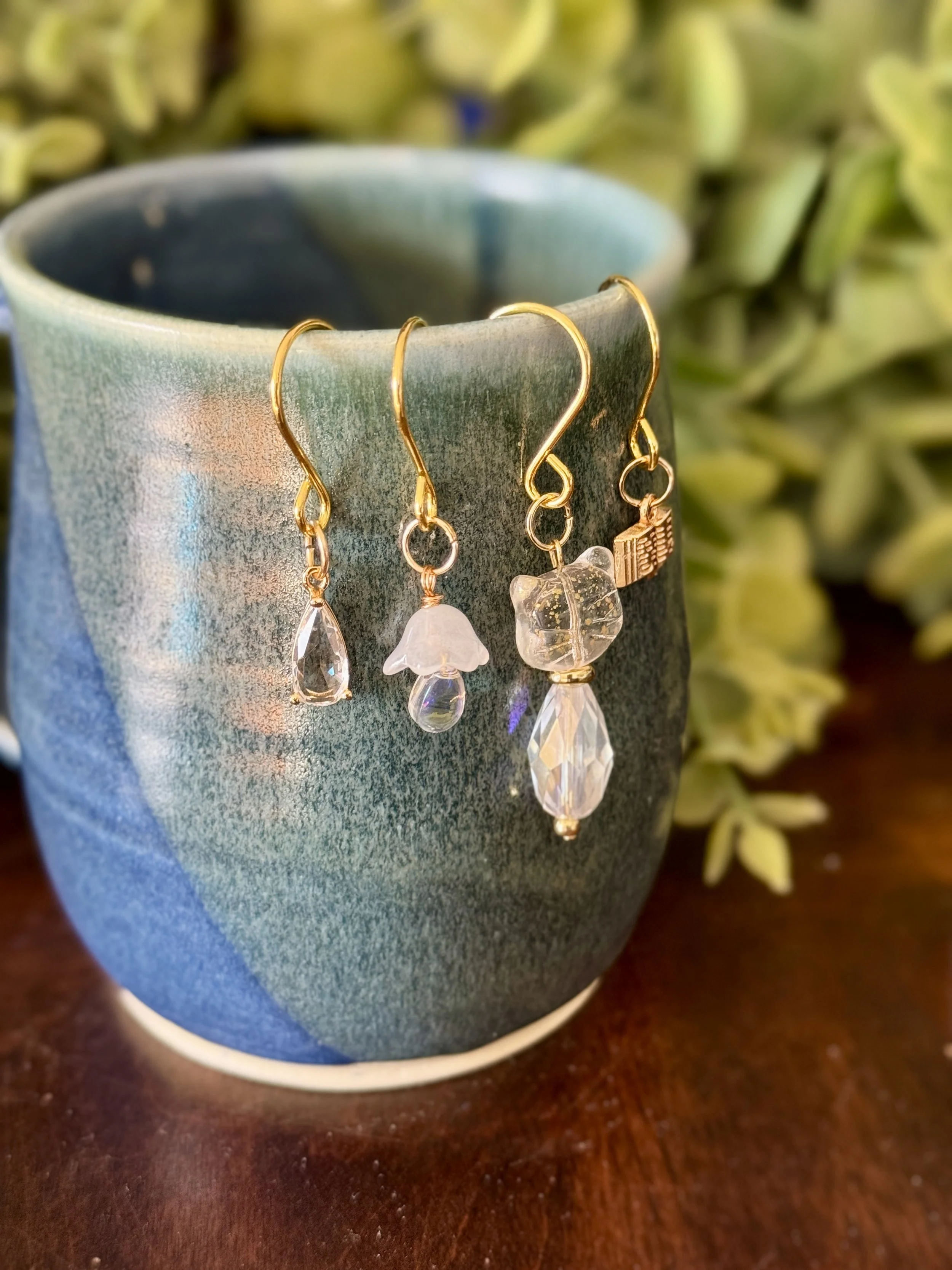 3rd Front View of White cat + white mushroom + book + crystal pendant plant charm set on a mug with a leafy background