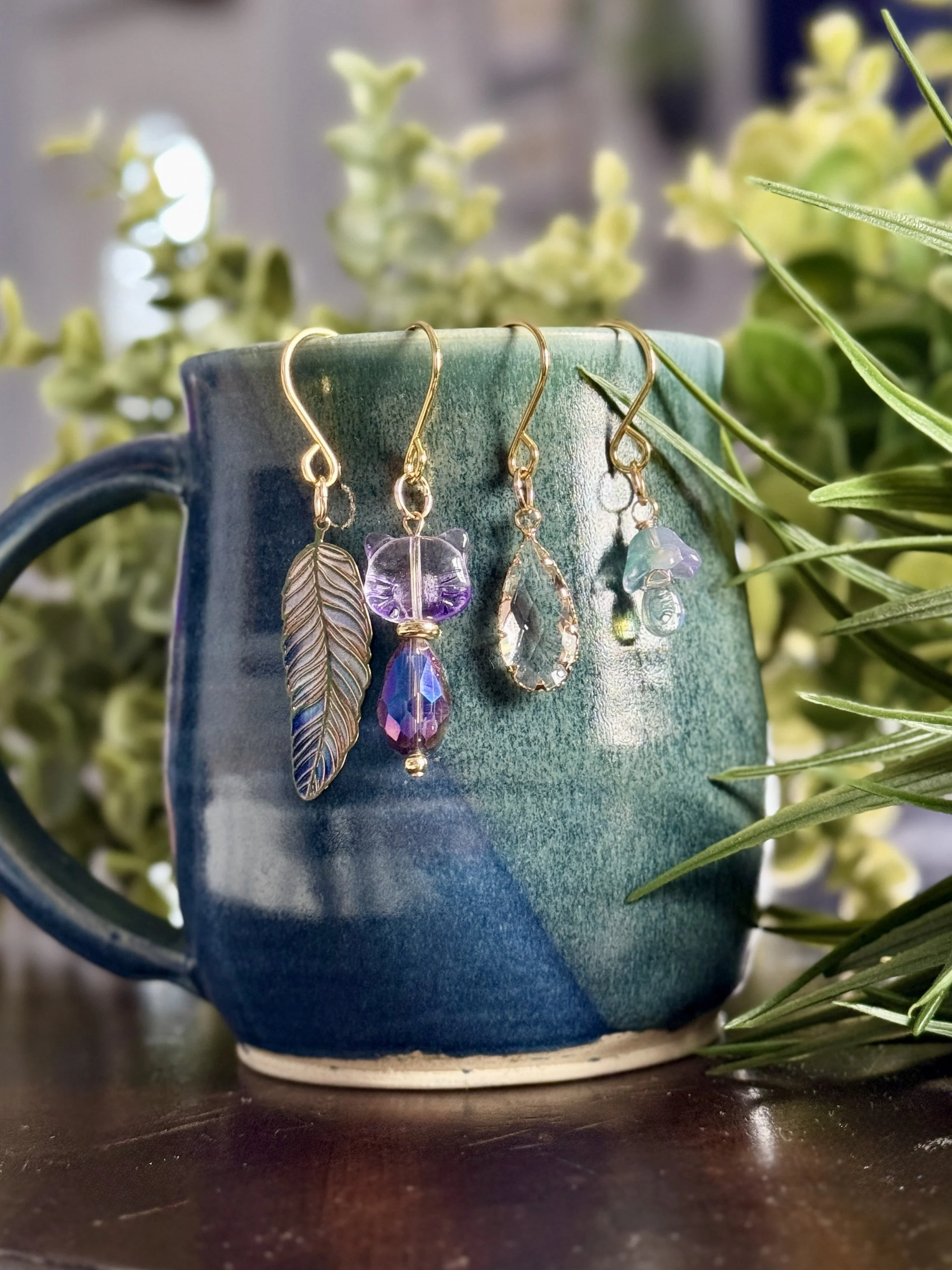 6th alternative front View of Purple cat + lavender mushroom + feather + crystal plant charms on a blue mug with leafy background