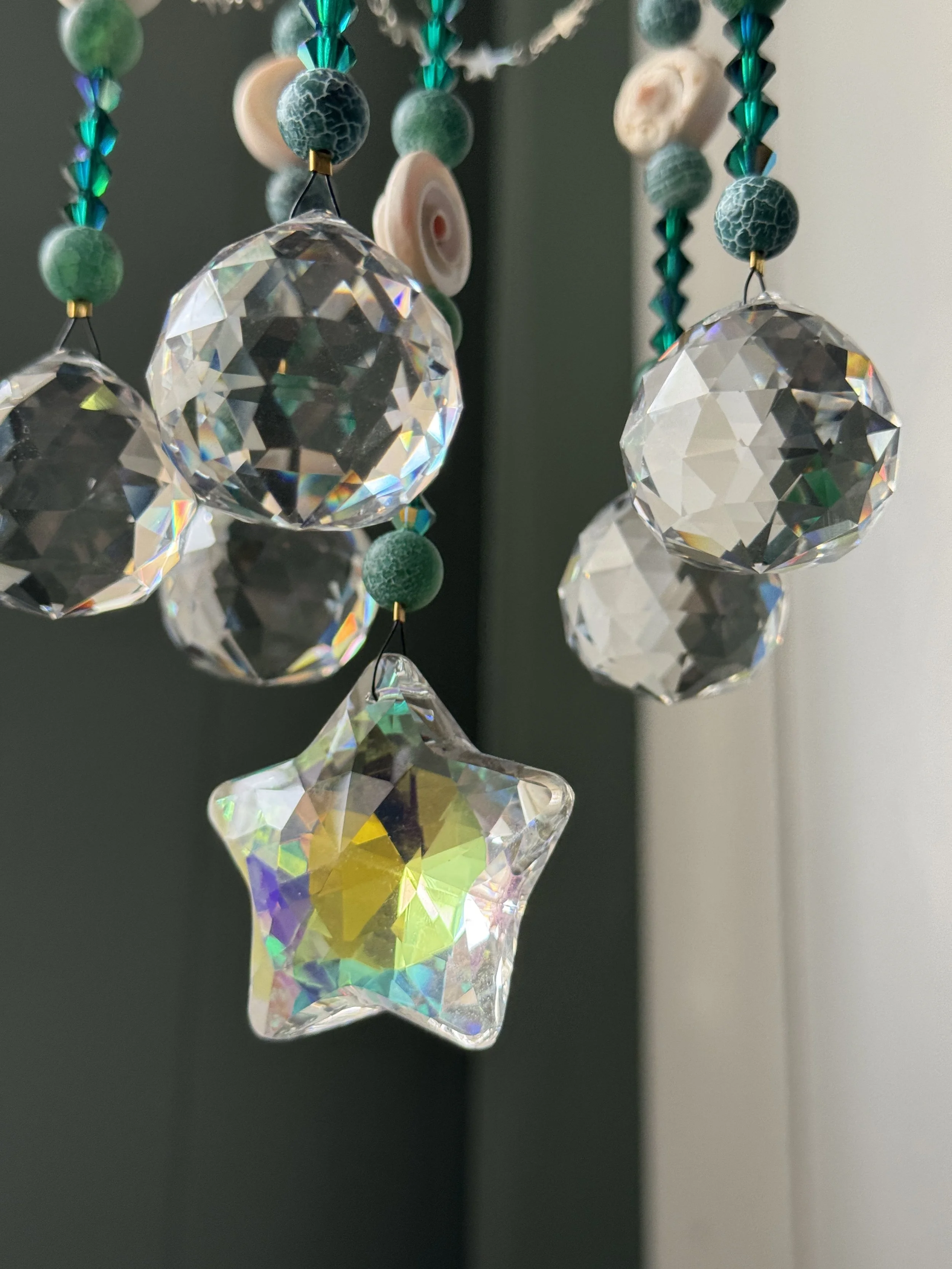 Close-up of a decorative hanging ornament with multicolored crystalline star and round beads, with a dark green and beige background.