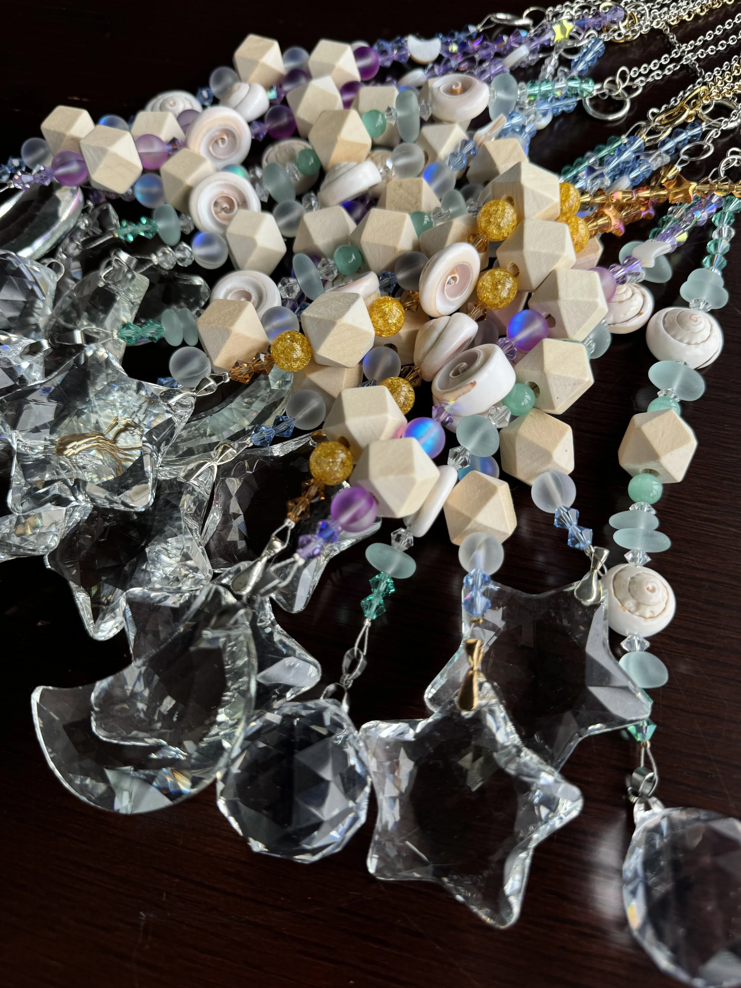 Close-up of colorful beaded jewelry with seashells, wooden beads, and crystal charms on a dark wooden surface.