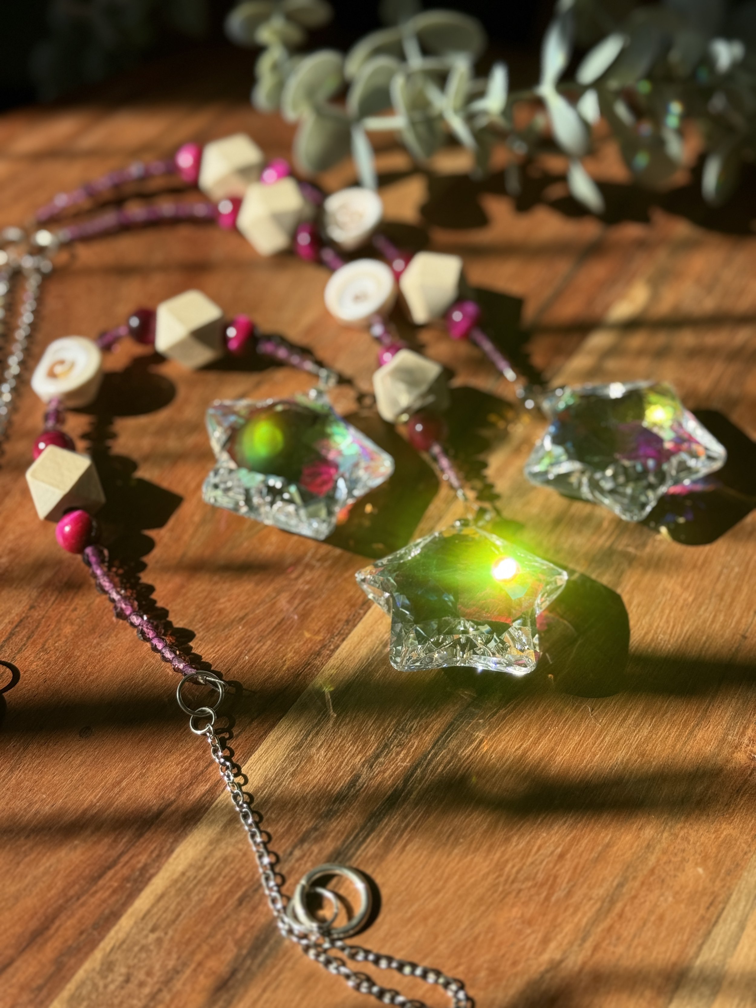Colored glass star-shaped ornaments and beaded necklaces on a wooden surface with sunlight creating reflections and shadows.