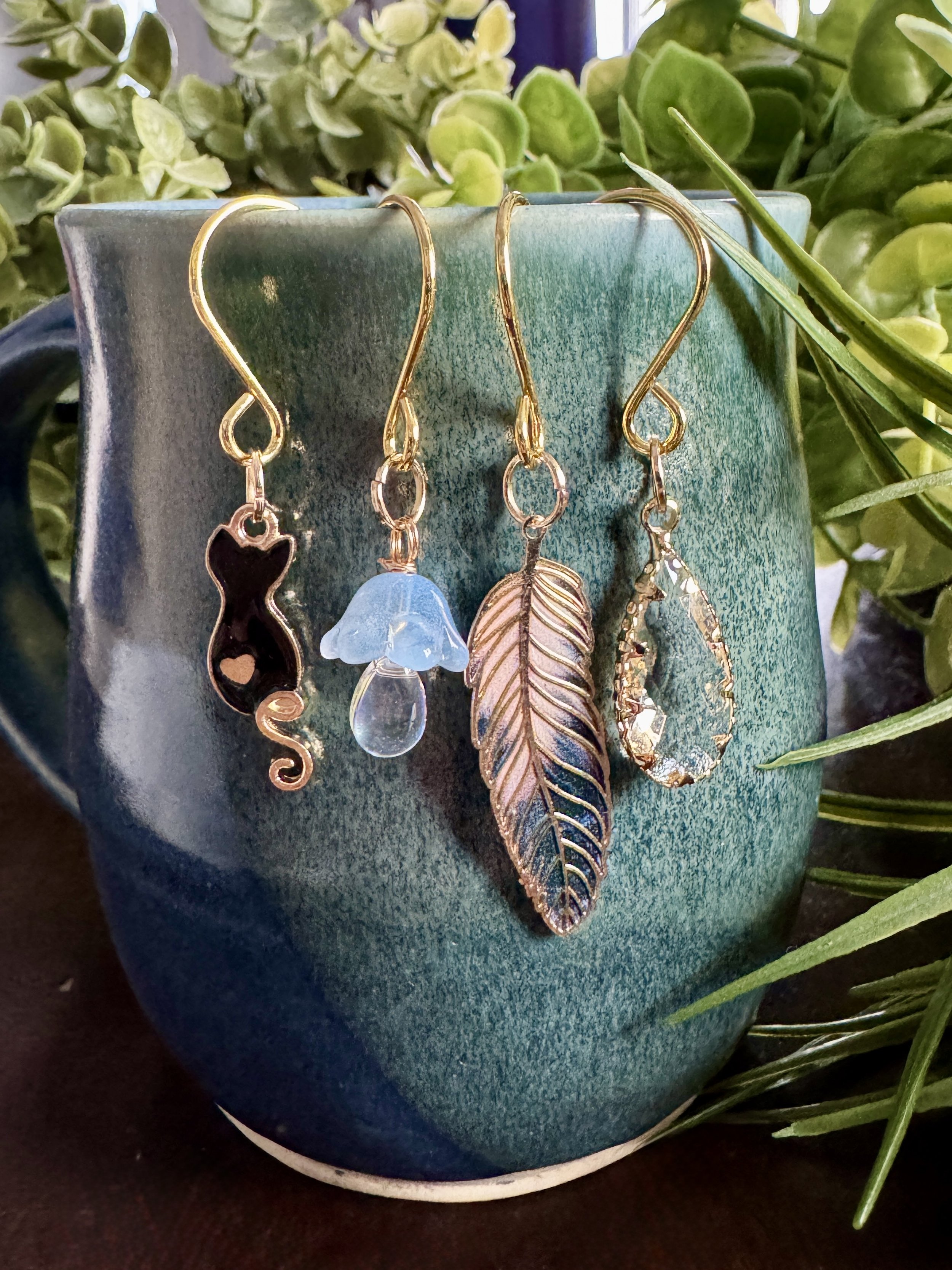 close up front view of Black cat + feather + mushroom + crystal plant charms on a leafy background