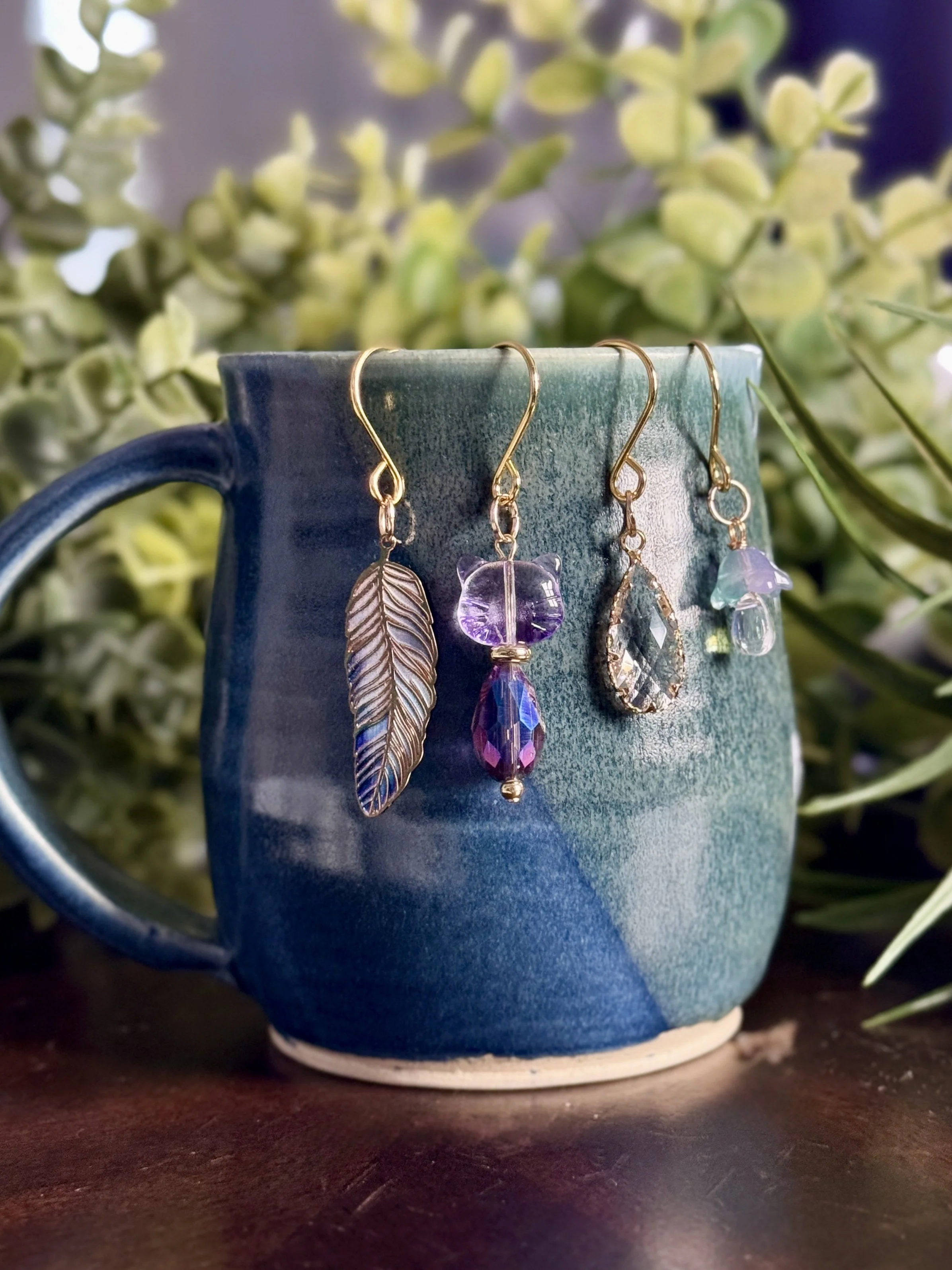 2nd alternative front View of Purple cat + lavender mushroom + feather + crystal plant charms on a blue mug with leafy background