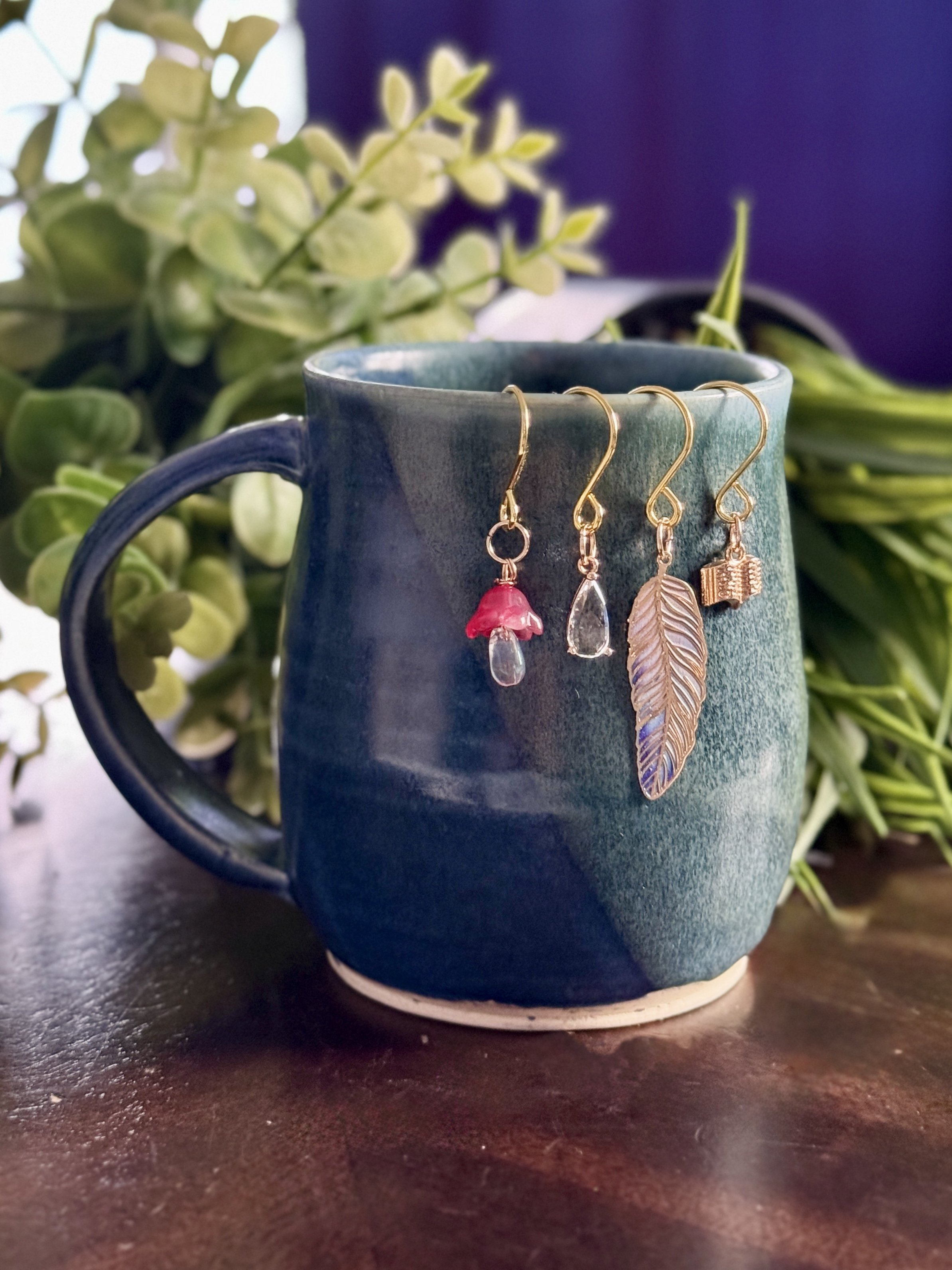 4th Alternative front view of a pink mushroom + book + feather + crystal plant charms hanging on a mug with leafy background