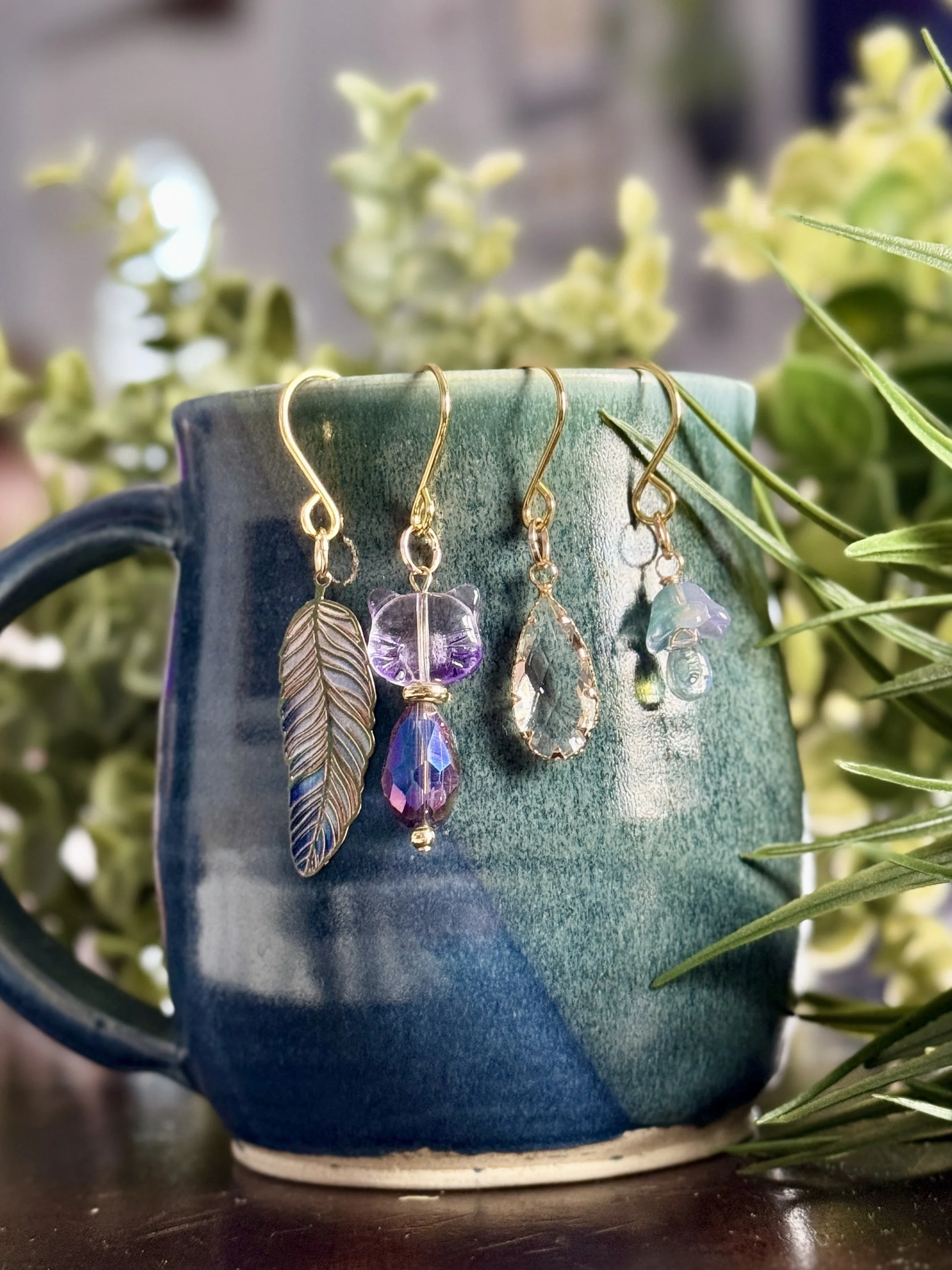 7th alternative front View of Purple cat + lavender mushroom + feather + crystal plant charms on a blue mug with leafy background