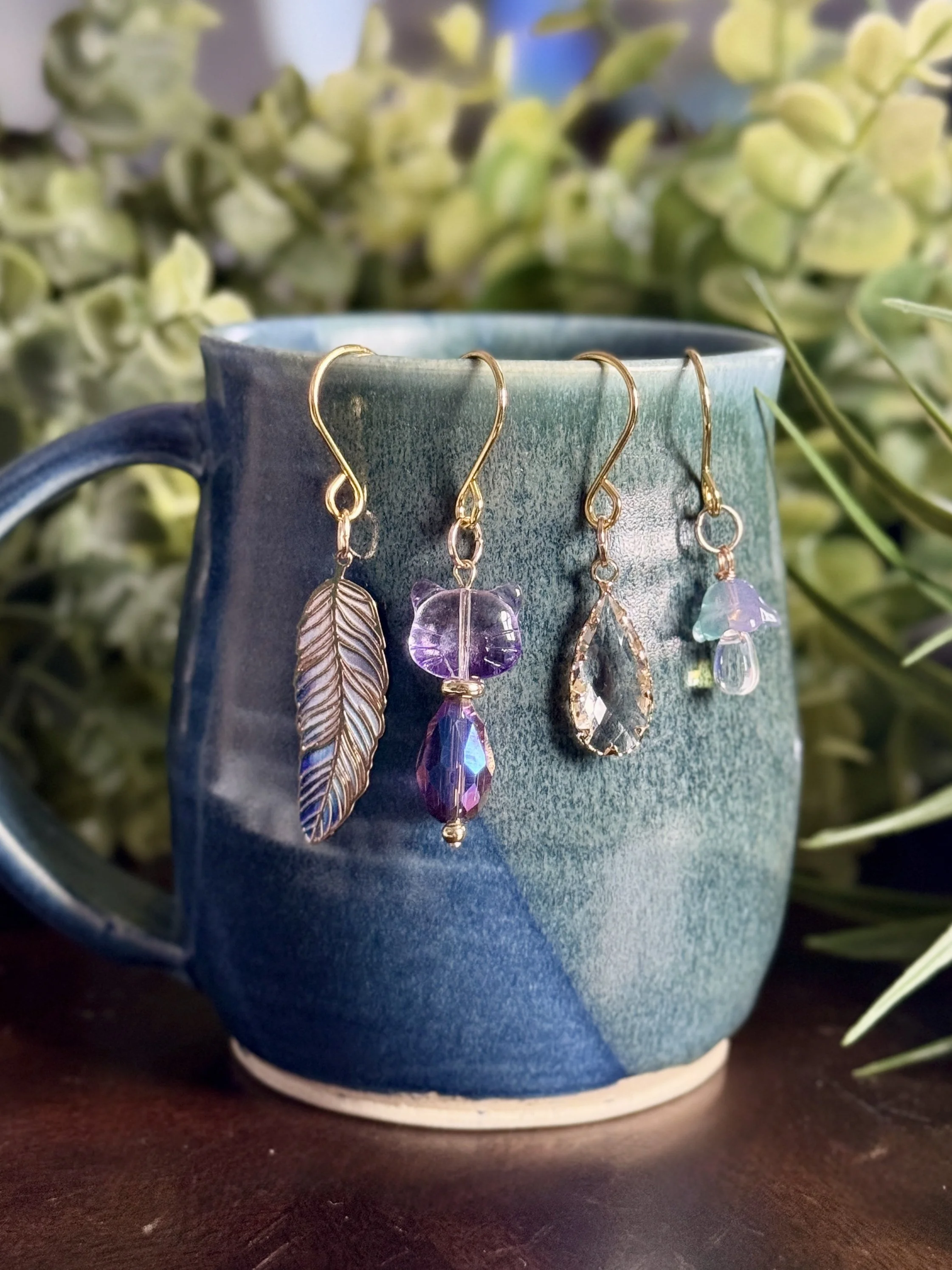 4th alternative front View of Purple cat + lavender mushroom + feather + crystal plant charms on a blue mug with leafy background