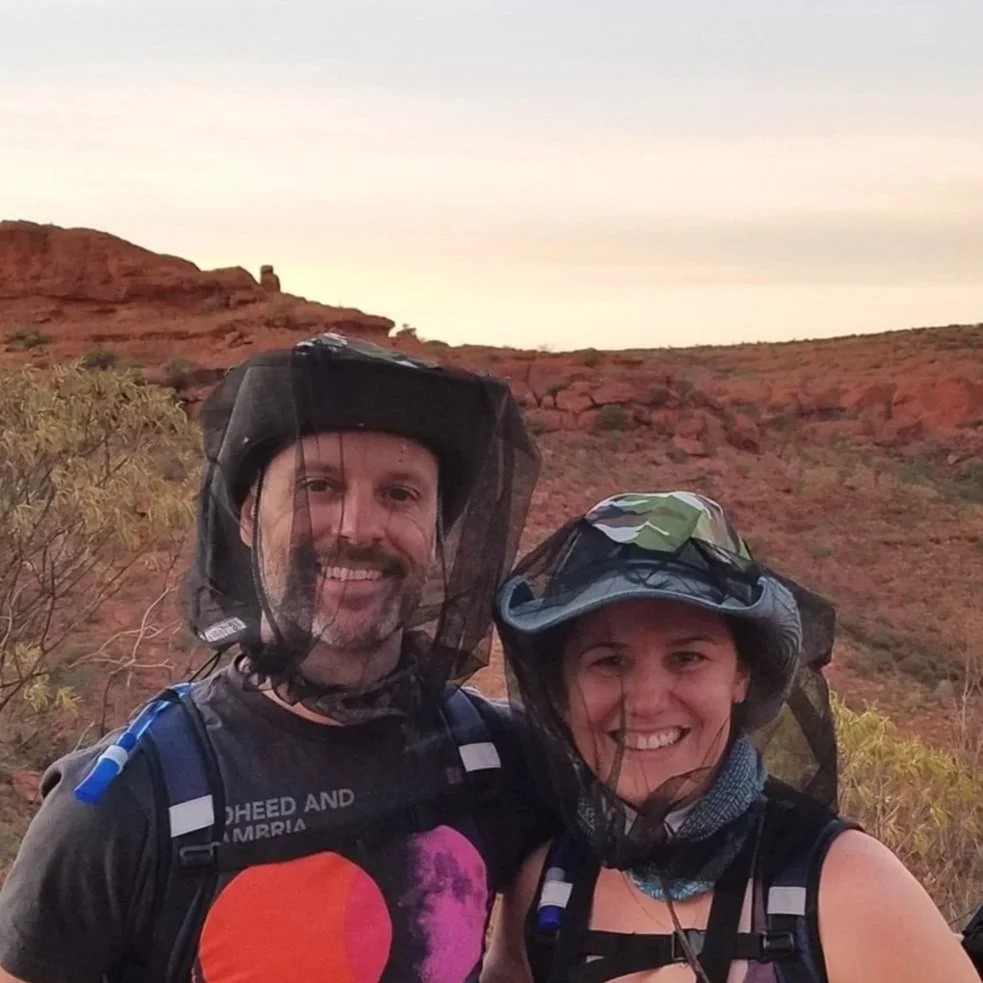 Chris and Michelle Coverdill wearing head nets at King's Canyon- a desert landscape with red rocks.
