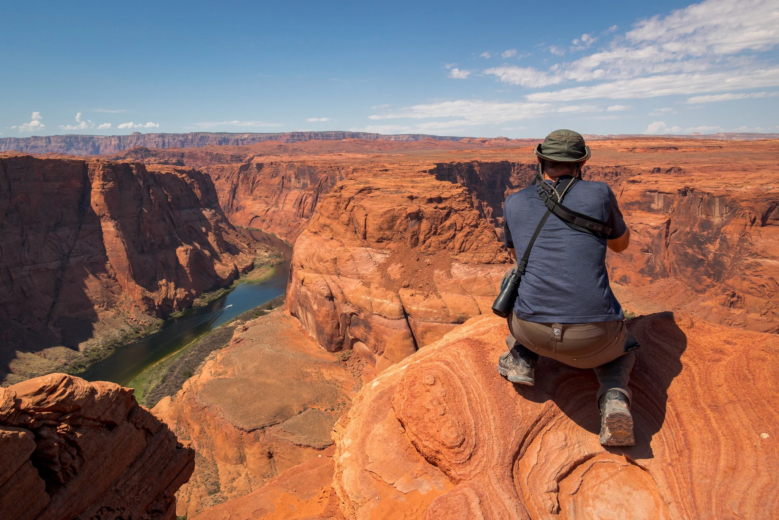 Chris Coverdill kneeling on the edge of red rocks at Horseshoe Bend, overlooking the Colorado River.
