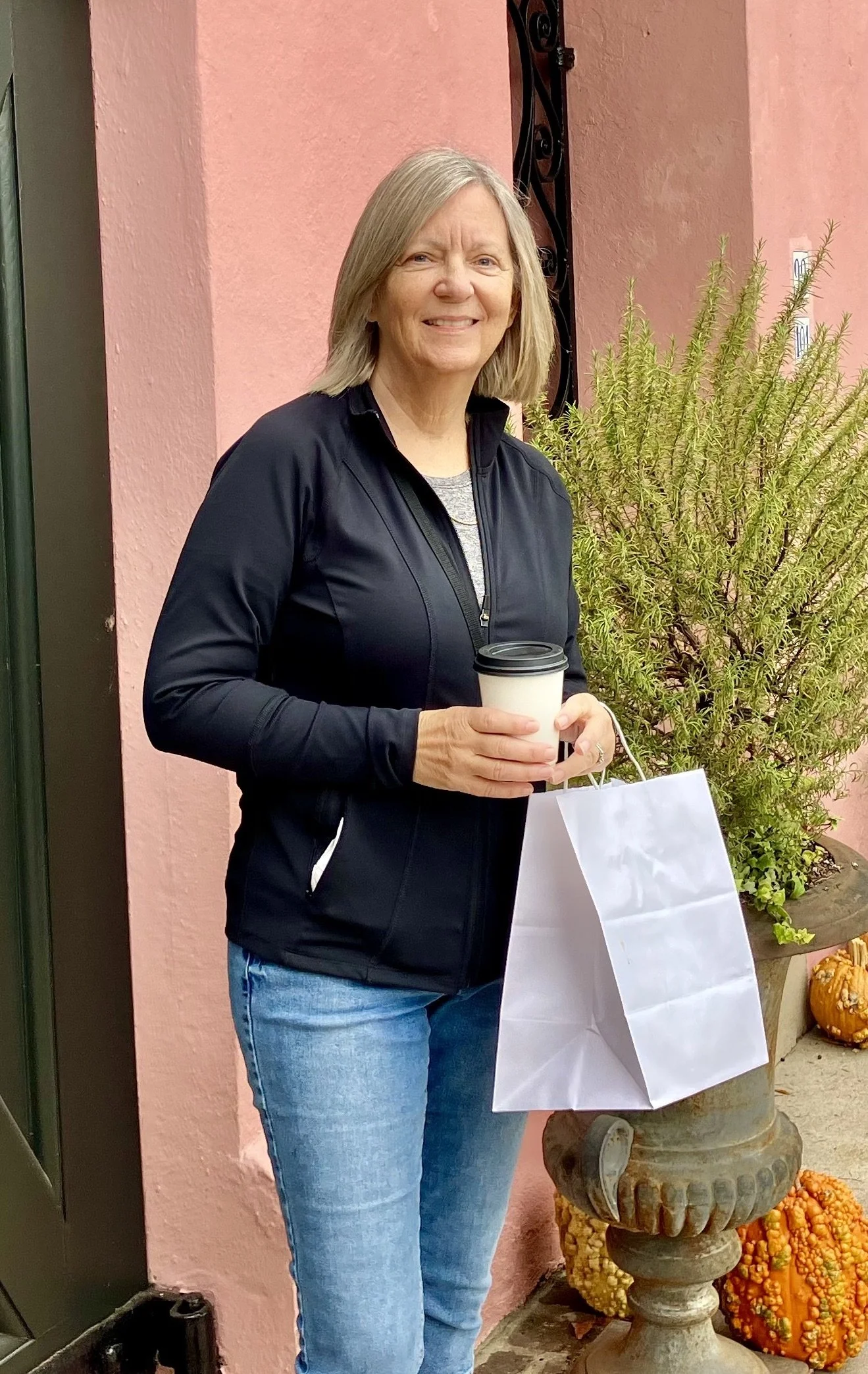 Woman wearing a green jacket standing on a wooden deck overlooking the ocean with trees in the background.