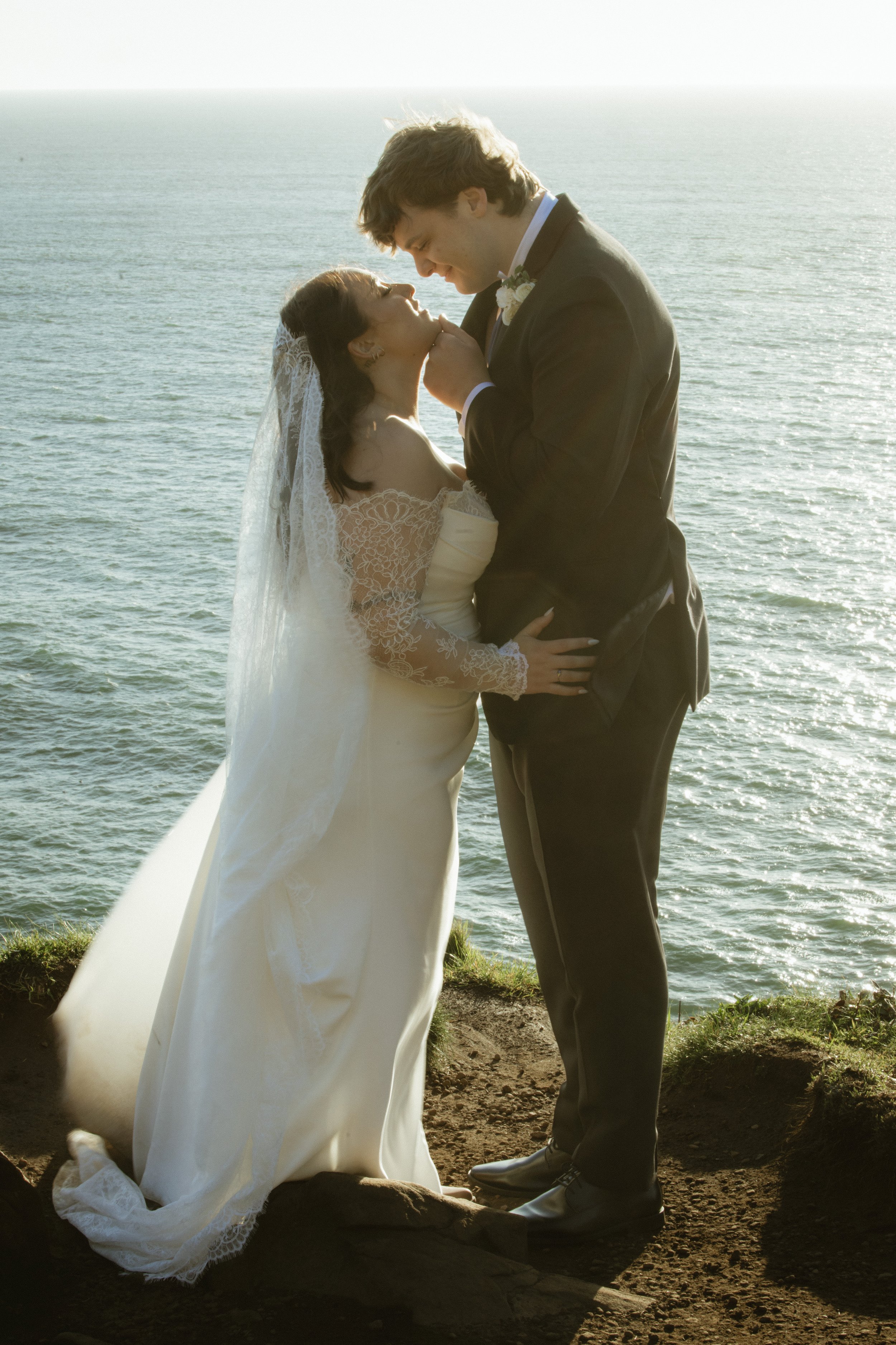 A bride and groom sharing a romantic moment on a cliffside overlooking the ocean.