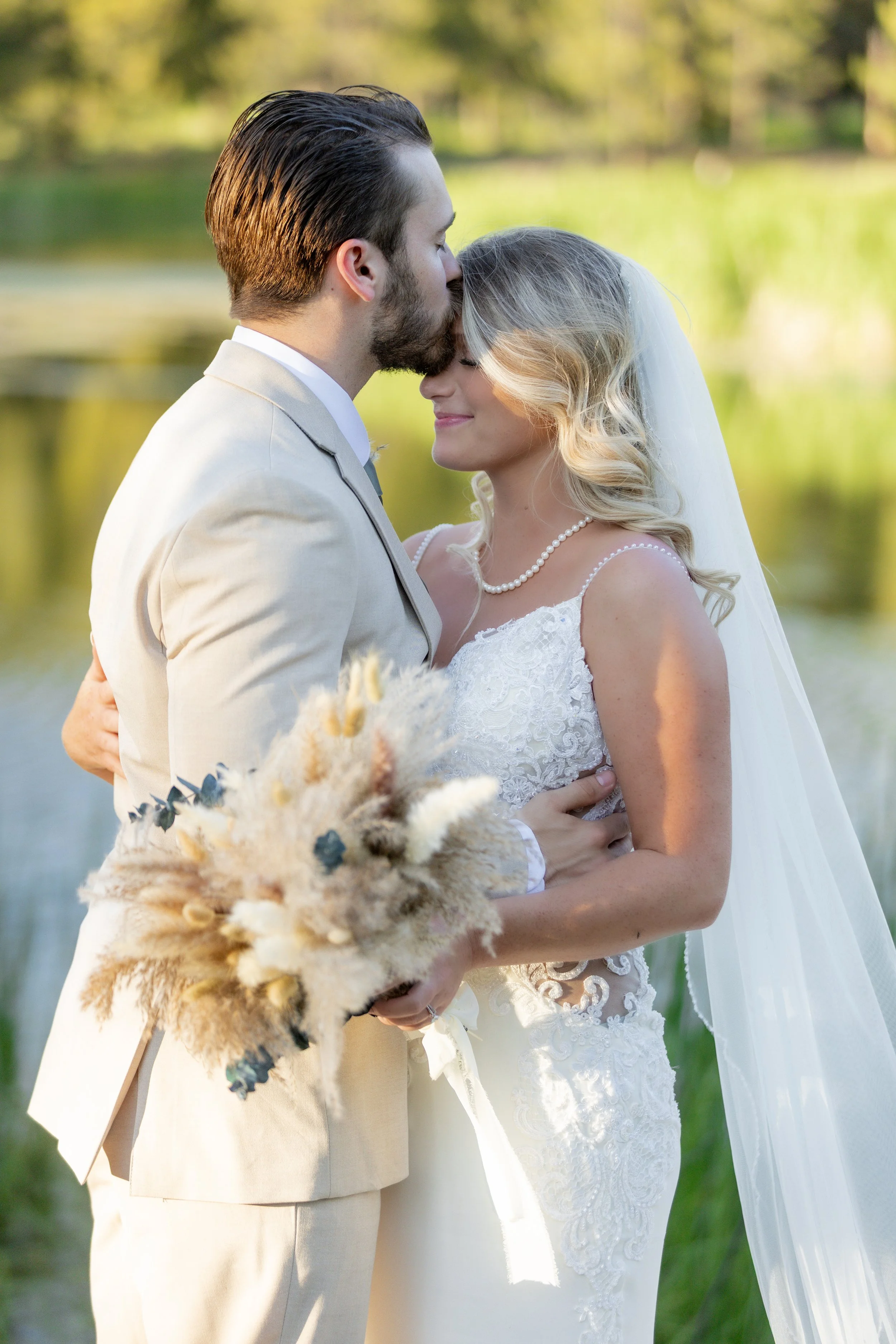 A bride and groom sharing a kiss by a lake with mountains in the background.