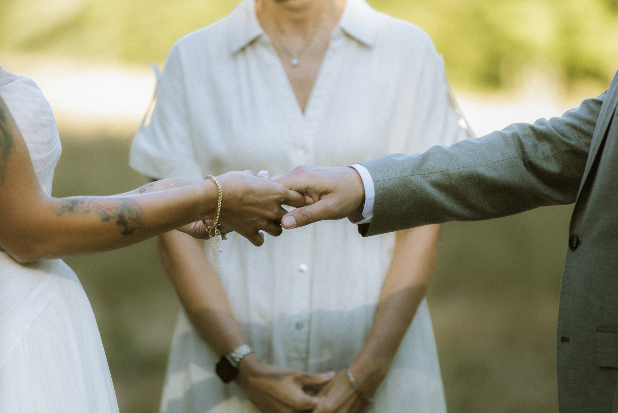 A couple holding hands during a wedding ceremony outdoors, with an officiant standing behind them.