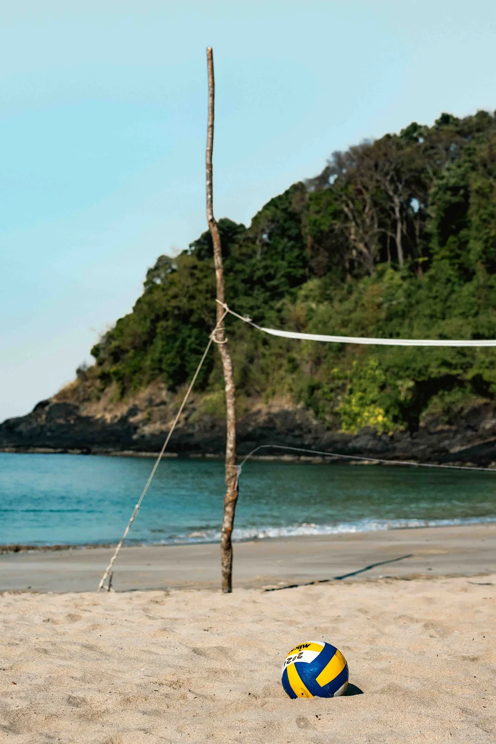  A volleyball placed in the sand of a beachvolleyball field with a mountain covered with trees of Ao Nui Bay in Koh Lanta. 