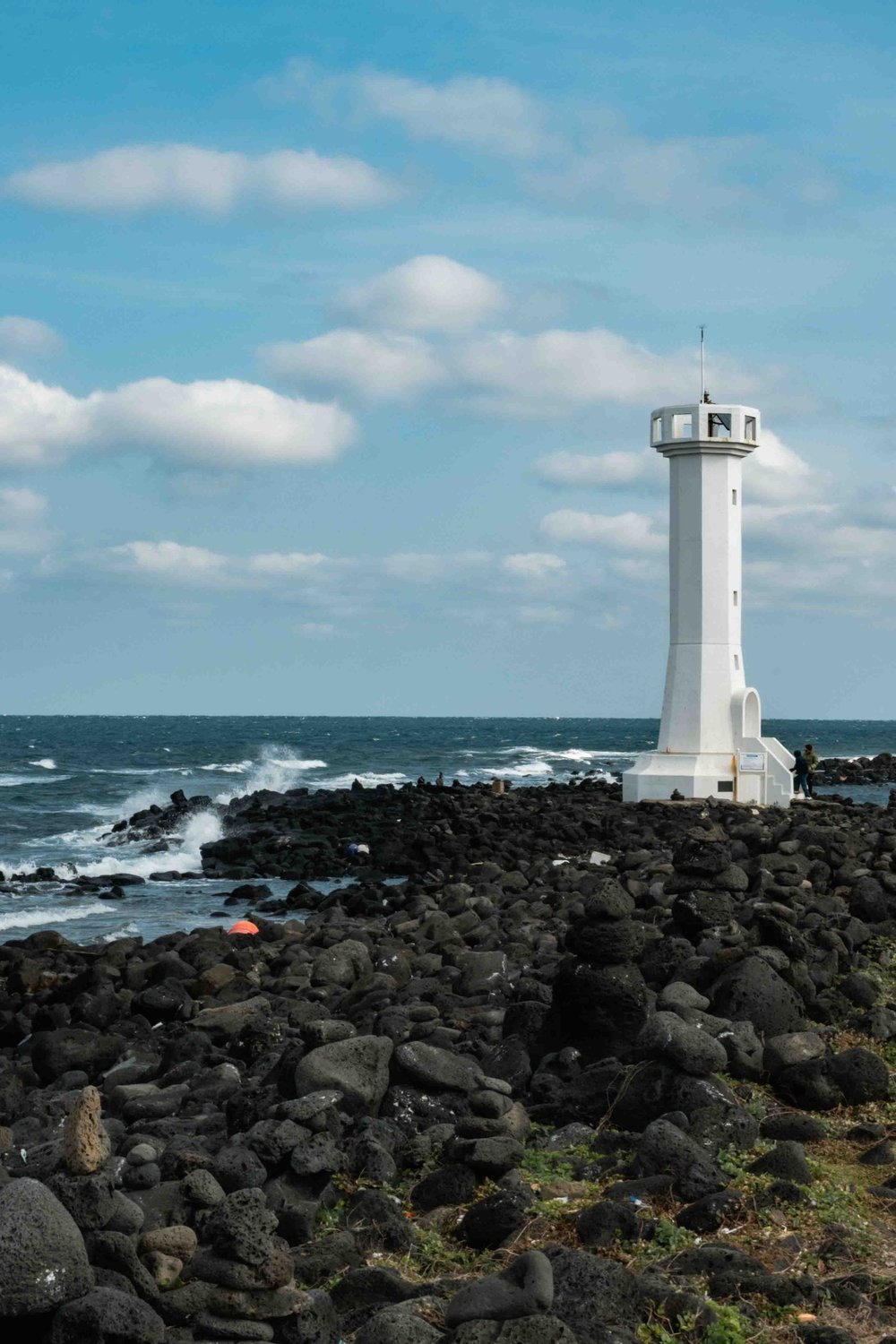  White lighthouse at the coast of Udo Island with black basalt rock and blue sky. 