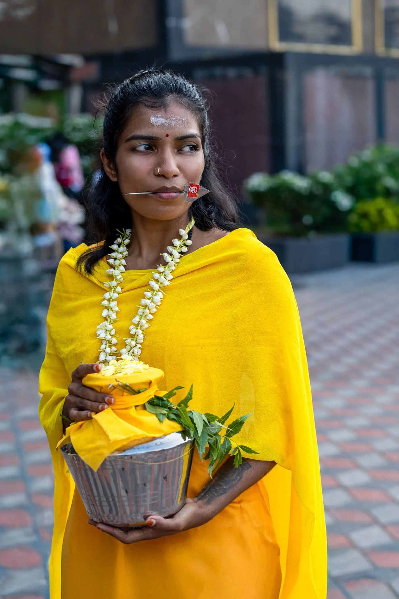 Malaysian girl dressed up Thaipusam in yellow & also wearing ornaments which are worn for poojas. She is holding a pot which is used for offerings at the Batu Cave temples.