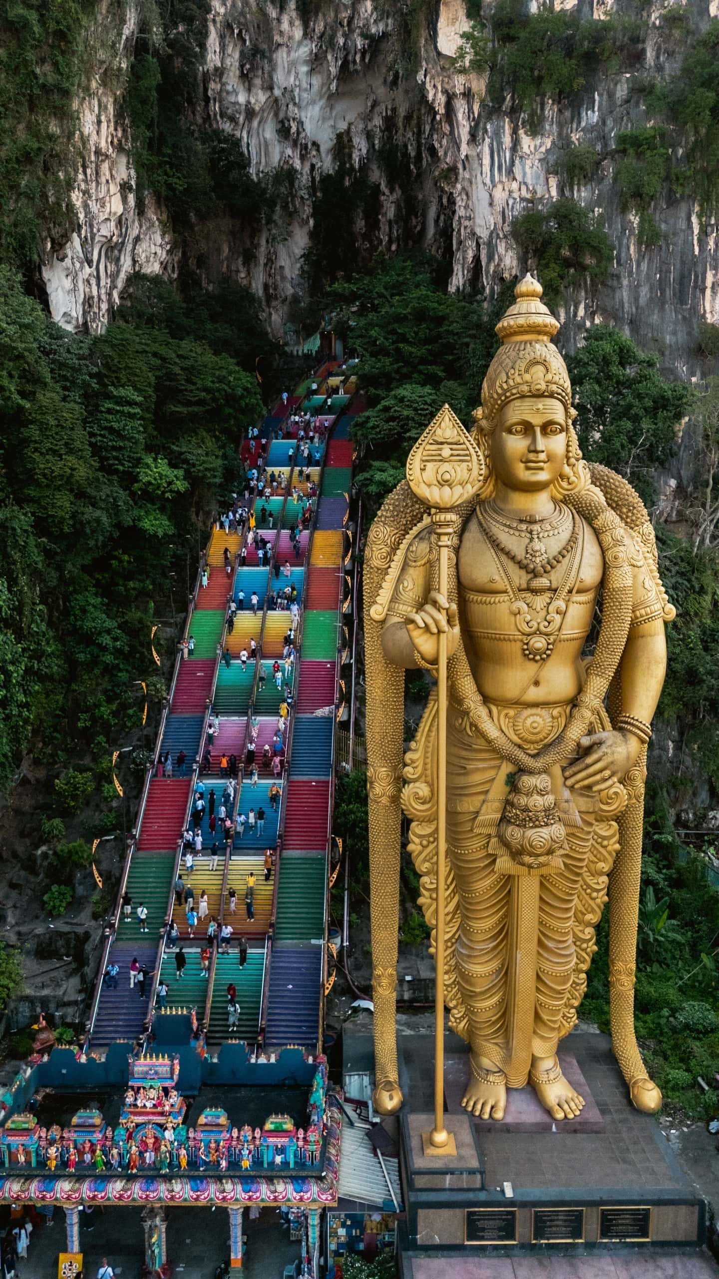 Tall Murugan statue standing besides the beautiful rainbow stairs leading to Batu Caves