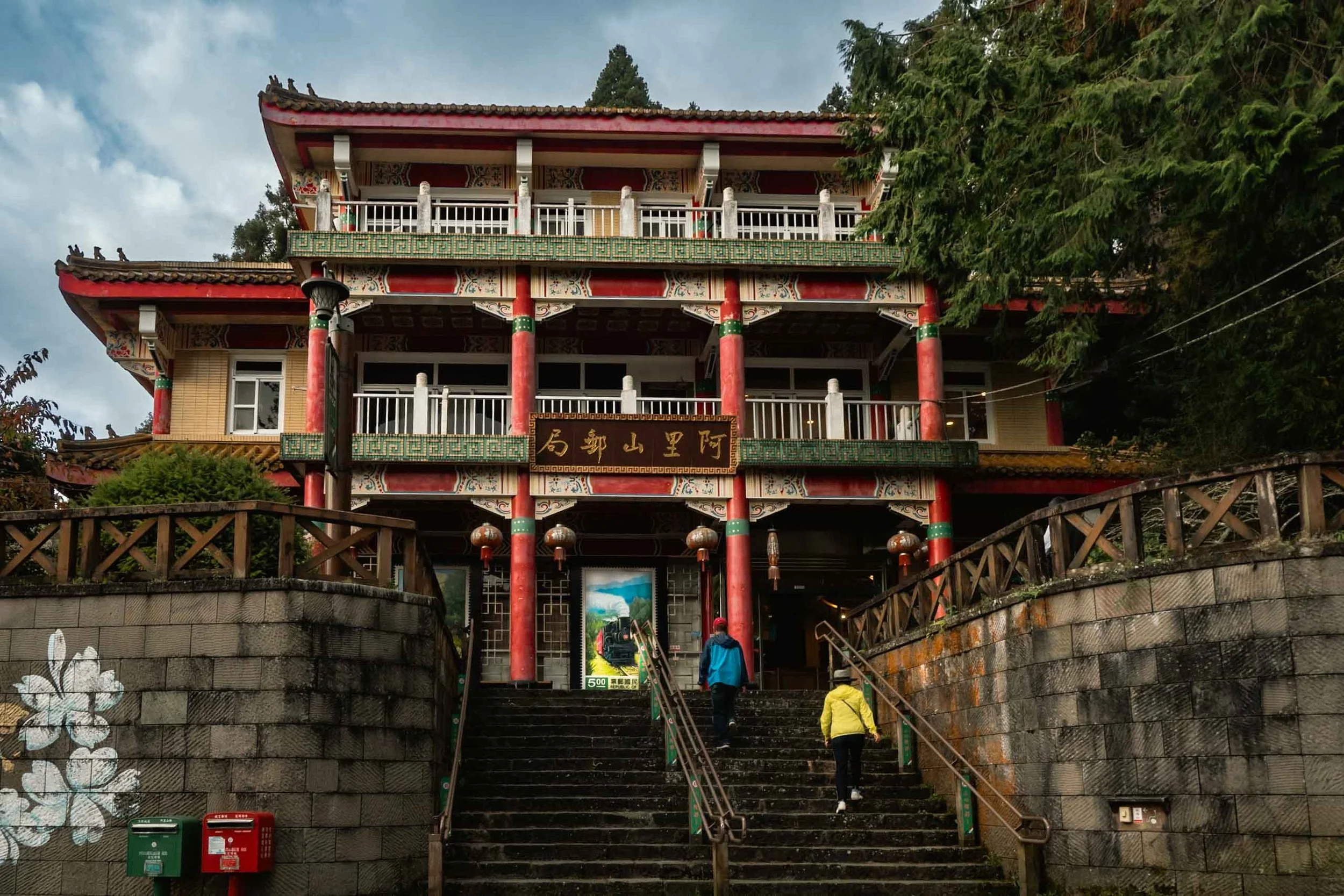 Two people walking up the staircase of the post office of Alishan with a traditional chinese design in red and green colors.