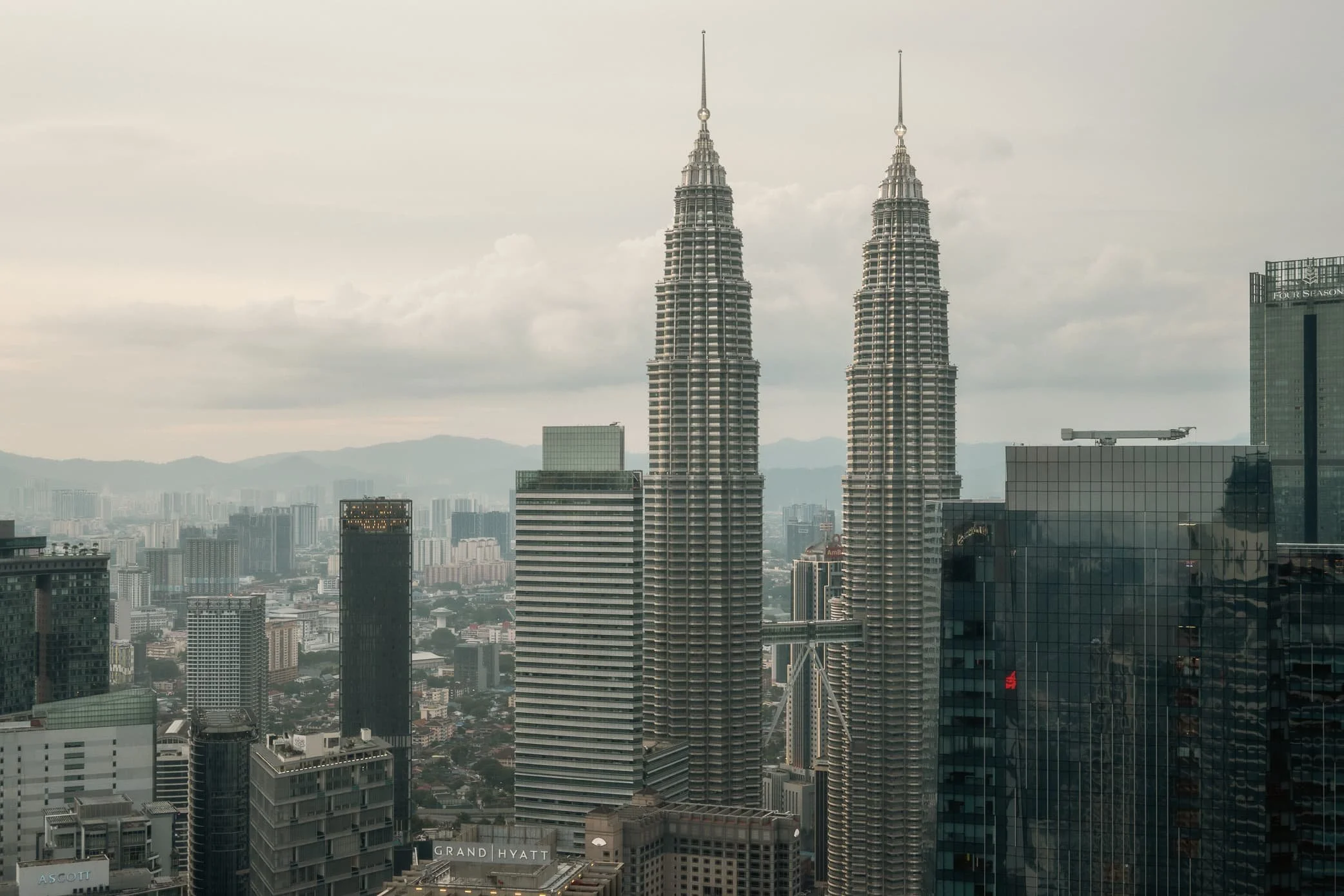 Iconic Petronas Twin Towers in Kuala Lumpur during daytime, with blue sky and surrounding skyscrapers.
