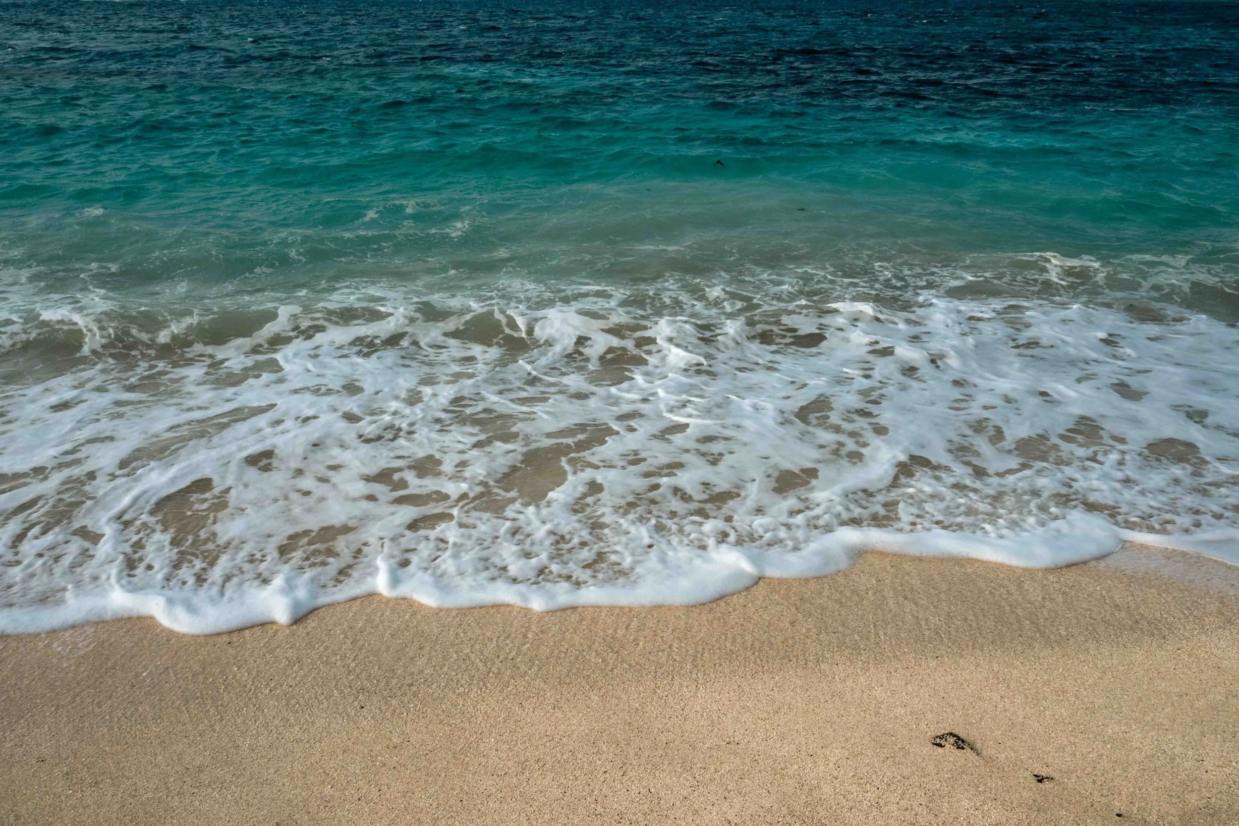 A wave from the turquoise ocean flushing with white foam onto the beach of Jeju island.
