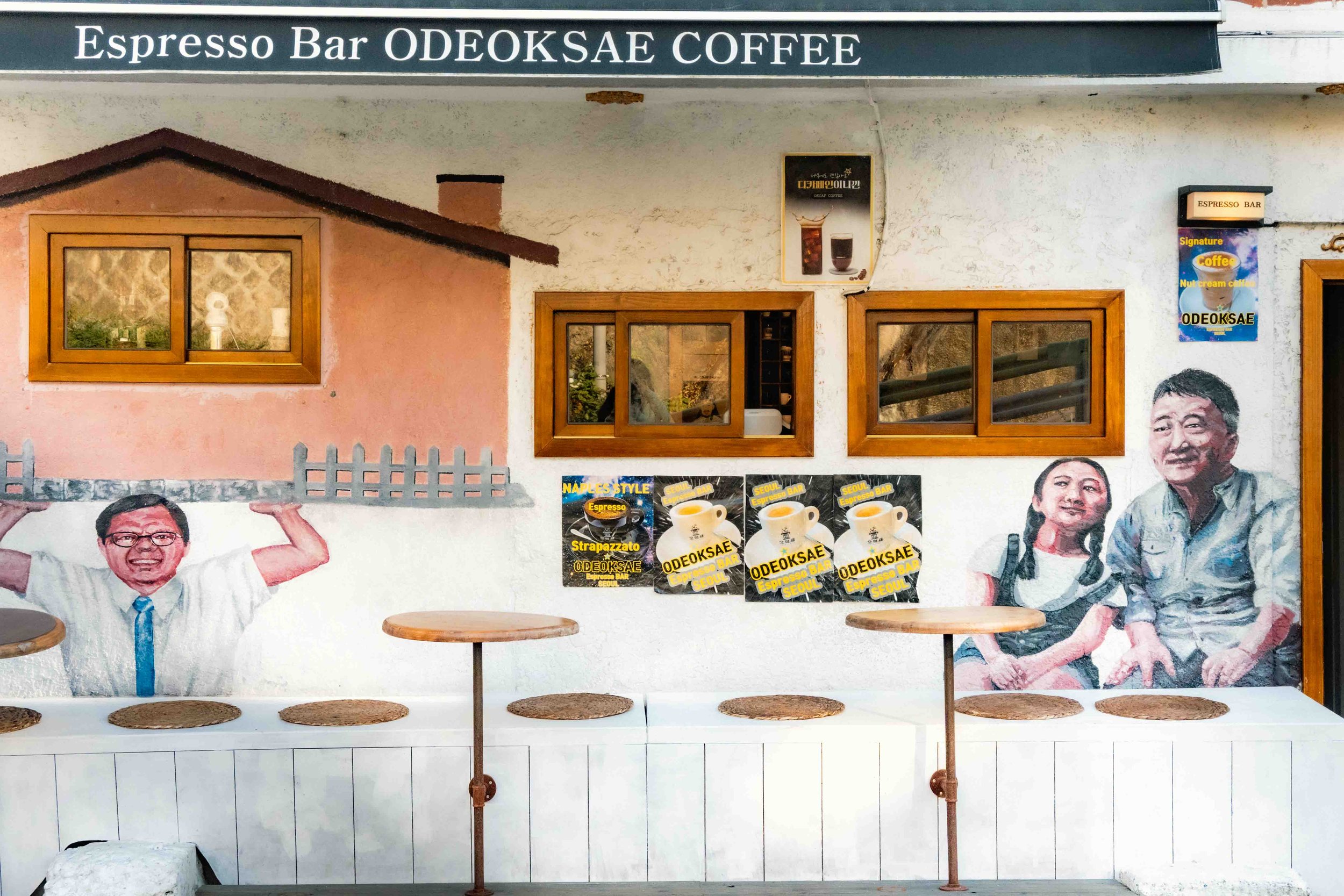 A mural displayed on a wall of a in the Ihwa Mural Village in Seoul displaying a father sitting next to his daughter waiting at a table to be served a coffee.