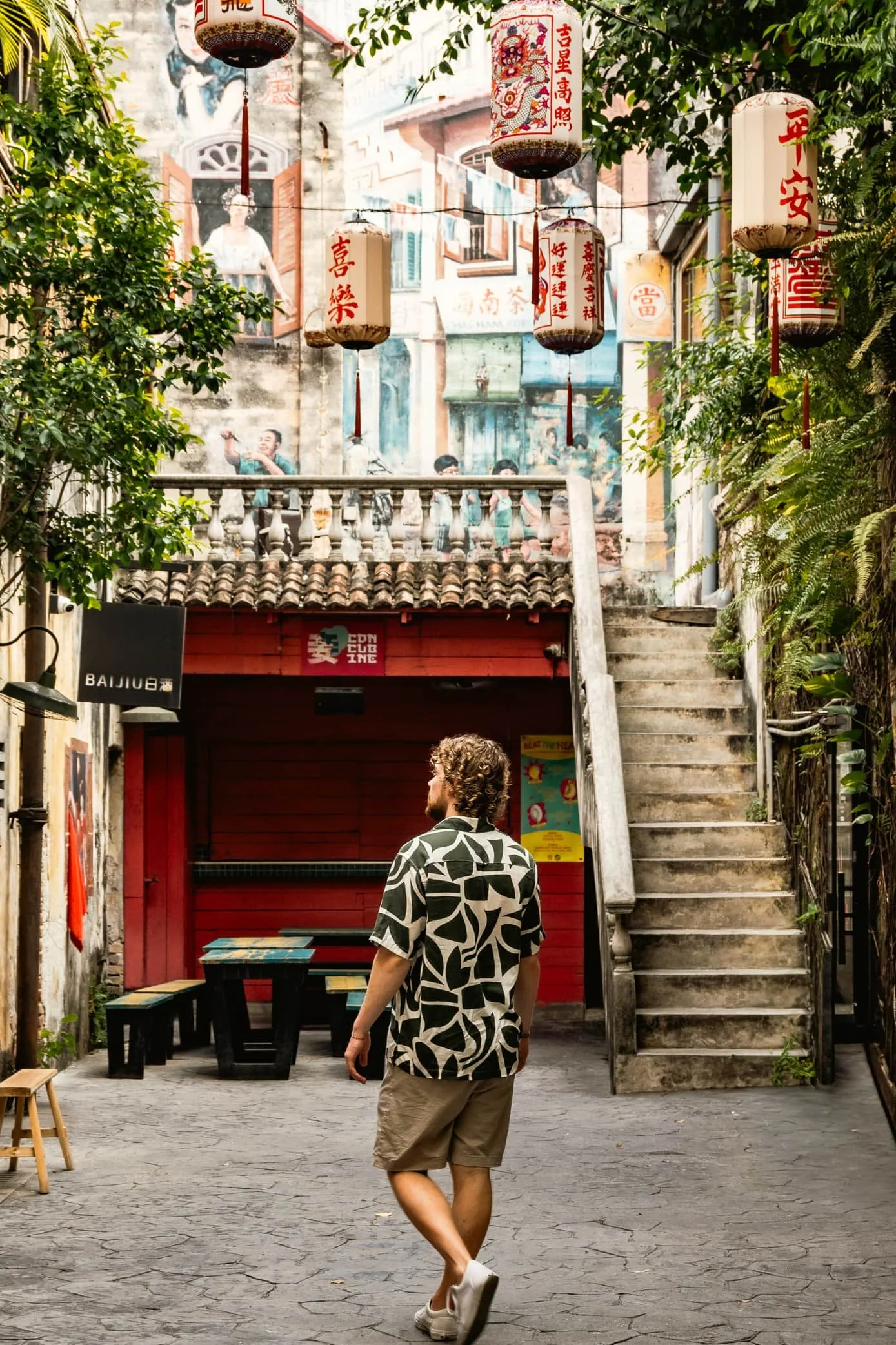 A male tourist posing in front of the vibrant murals and lantern displays at Sai Kwai Chai Hong, a restored heritage lane in Kuala Lumpur, Malaysia.