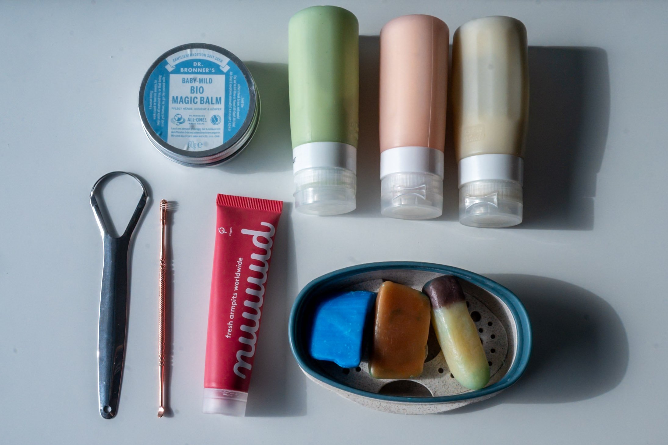Different eco-friendly toiletries like refillable bottles, solid soap, natural deodorant and body balm in a metal tin.