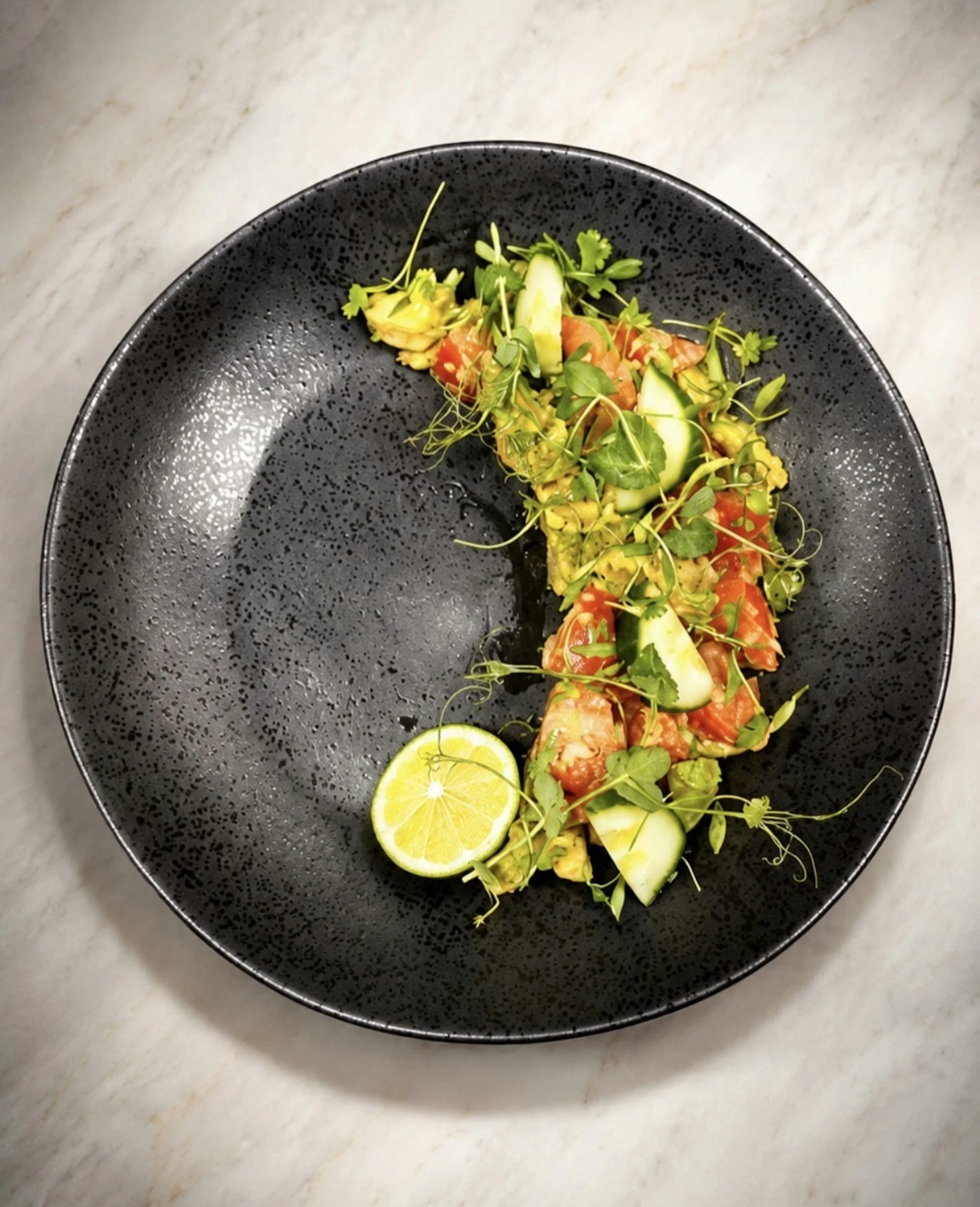 Crab, avocado, tomato and cucumber salad with lime on a dark plate