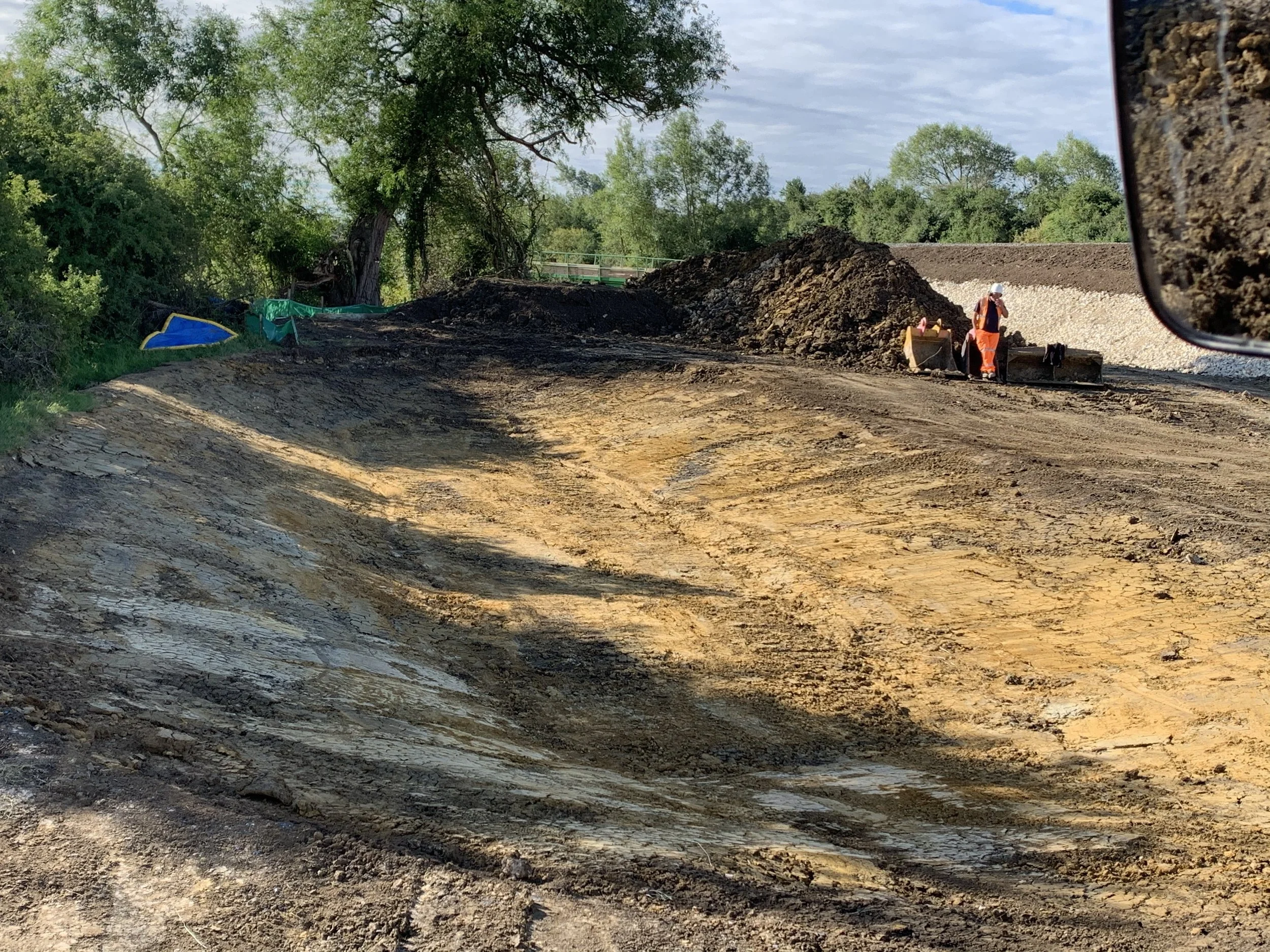 Habitat creation in progress showing a large excavated area with exposed earth layers, machinery, and construction workers preparing the site for ecological landscaping and biodiversity enhancement.