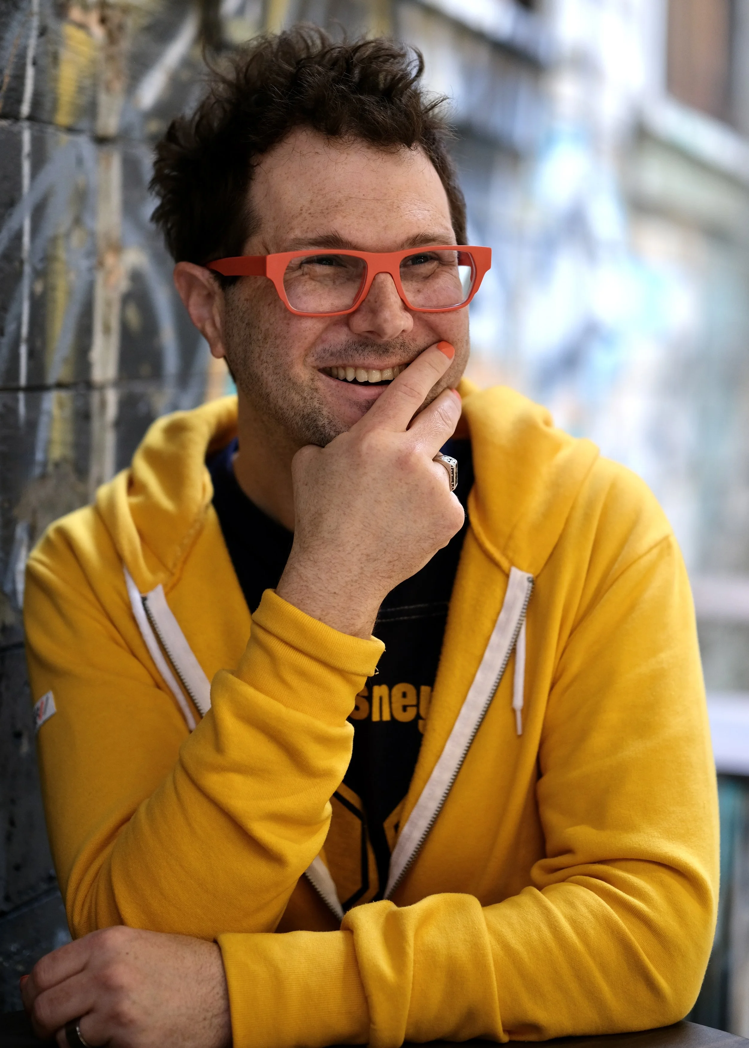 Photo of Barry Kudrowitz with orange glasses, yellow hoodie, and Disney shirt