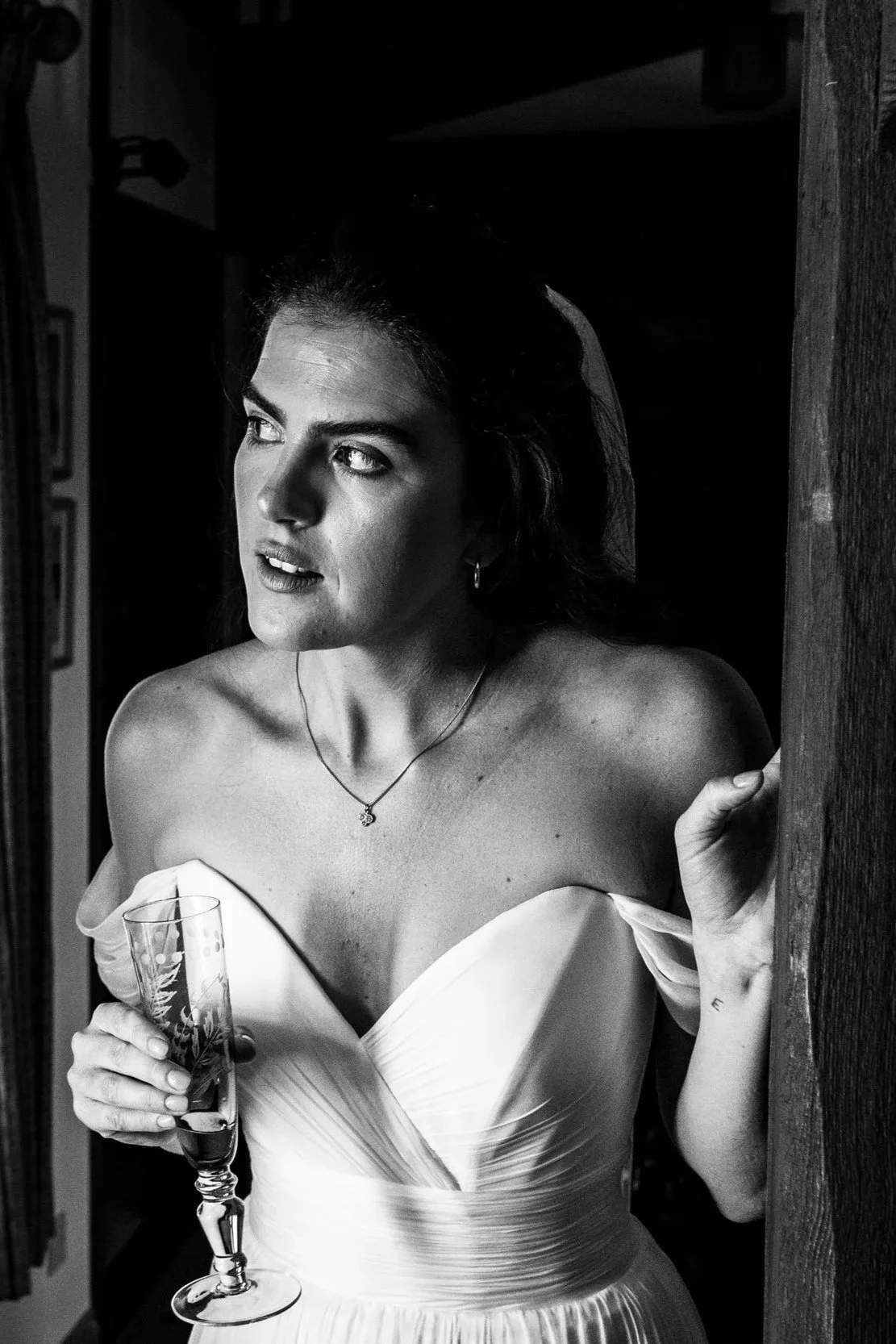 Bride in white dress holding champagne glass near window