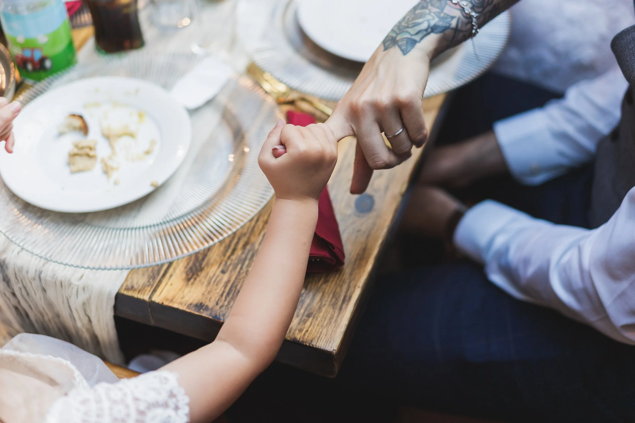 Child and adult holding hands at a dining table with partially eaten food and drinks.